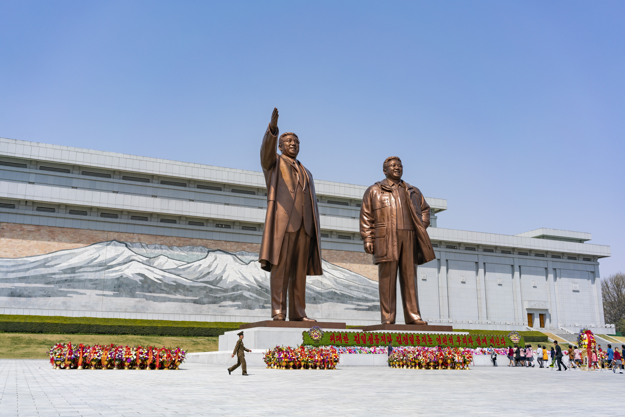  A North Korean soldier walks in front of the bronze statues of former North Korean leader Kim Il Sung and Kim Jong Il in Mansu Hill, Pyongyang, while citizens pay tribute bringing flowers on the birthday anniversary of the Eternal Leader. 