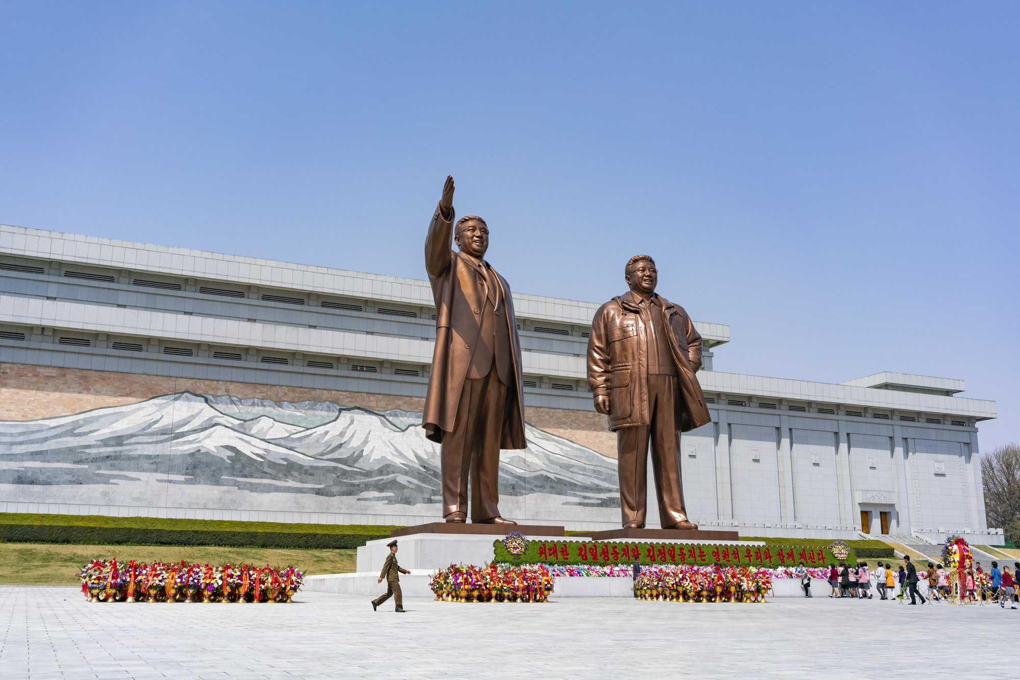 A North Korean soldier walks in front of the bronze statues of former North Korean leader Kim Il Sung and Kim Jong Il in Mansu Hill, Pyongyang, while citizens pay tribute bringing flowers on the birthday anniversary of the Eternal Leader.
