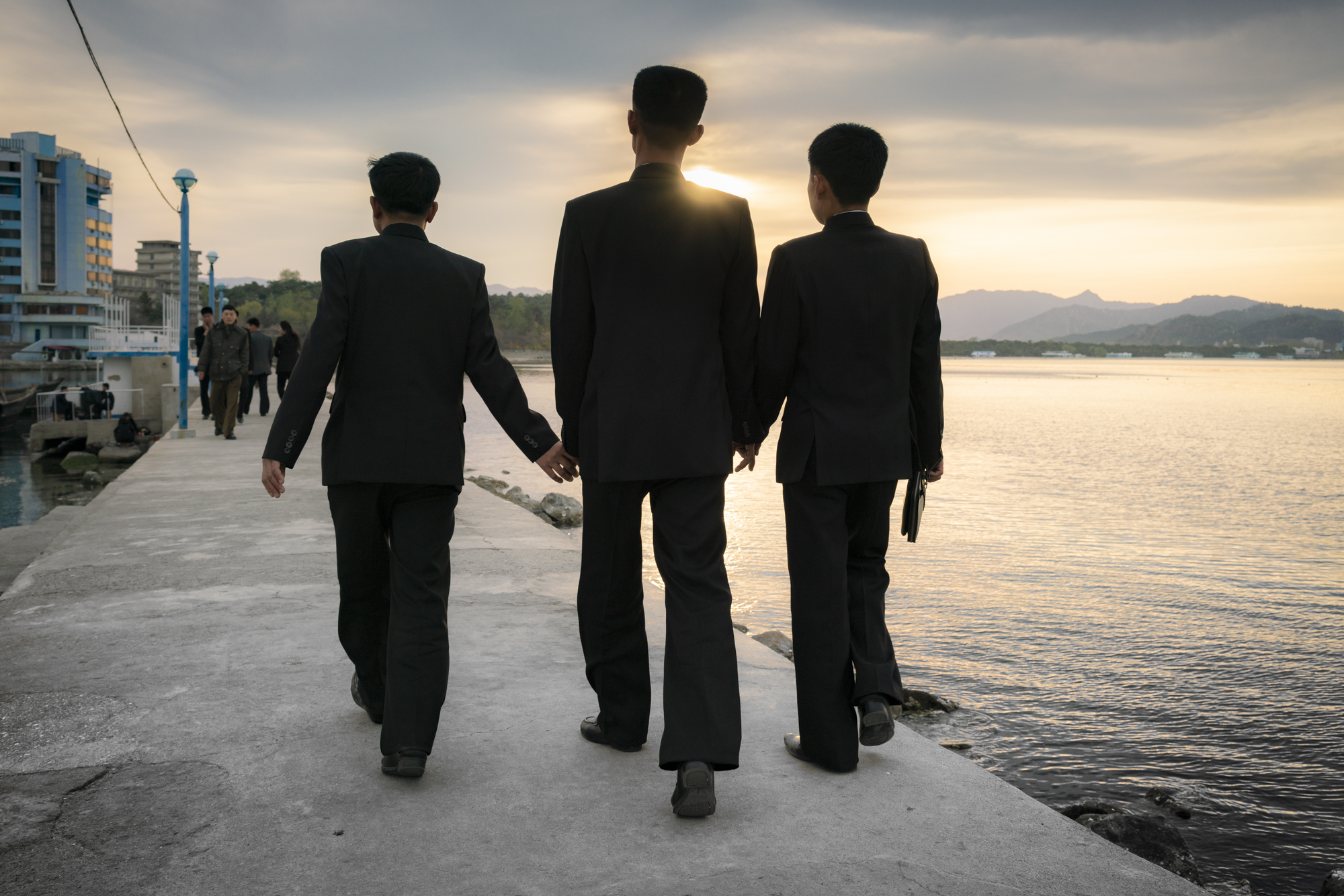  As the sun sets behind the hills, three North Korean students hold hands on the pier that connects the Wŏnsan docks to Jangdok Islet. 