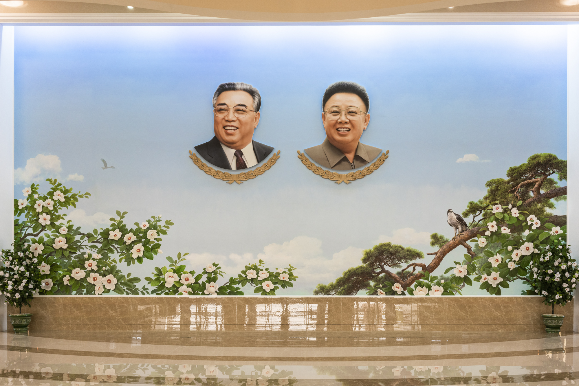 Cut out portraits of the North Korean former Leaders on a huge wall-painting depicting the national symbols – a northern goshawk and the magnolia flower, chosen for the purity perceived by its white colour.