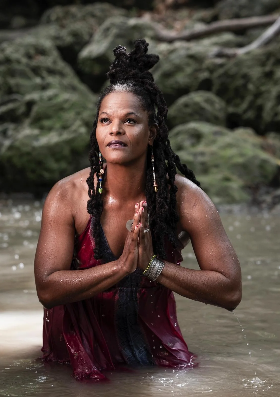 Caribbean woman sitting serenely in water, hands in prayer, gazing upward with a solemn, peaceful expression, embodying grace, spirituality, and wisdom