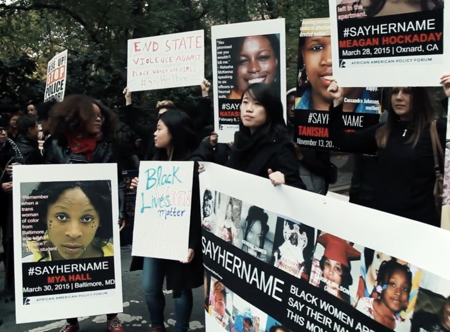 Image: Film still of protestors holding signs that say "Black Lives Matter" and "Say Her Name"