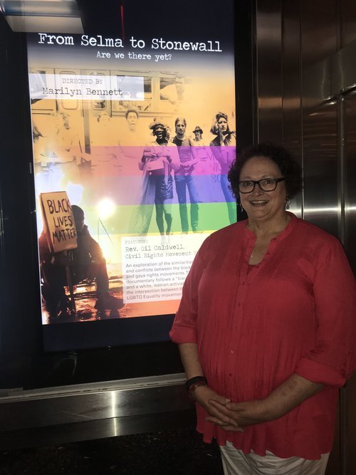 Image: Photo of Marilyn Bennett in front of the film poster for From Selma to Stonewall at the New York City Out Cinema film festival 