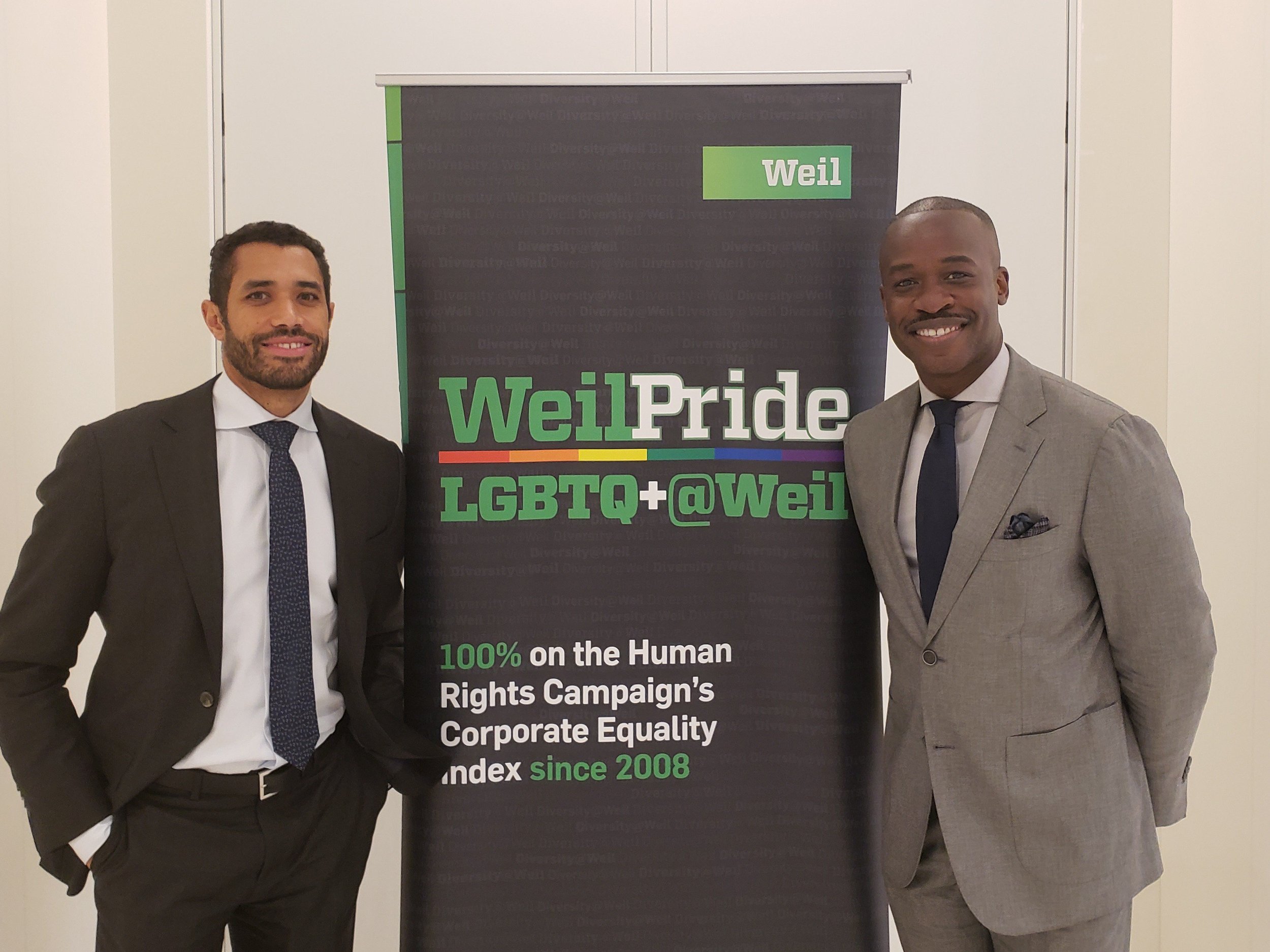 Image: Photo of two Weil, Gotshal, and Manges employees in front of a banner