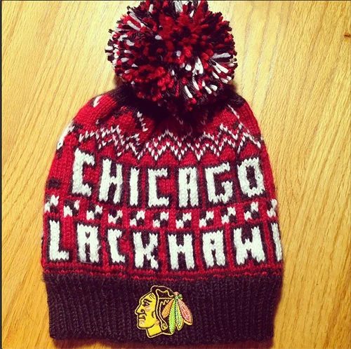 A red knit beanie hat with a pom-pom on top, featuring the text 'CHICAGO BLACKHAWKS' and their logo on the front.