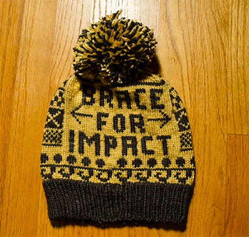 Yellow knit beanie hat with black patterns and a pom-pom on top, placed on a wooden surface.