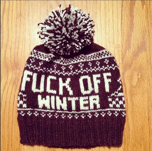 A knitted winter beanie hat with a pom-pom on top, featuring patriotic colors and patterns, and the phrase 'FUCK OFF WINTER' displayed on the front.