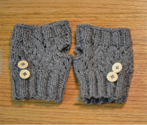 Pair of gray knitted fingerless gloves with two small white buttons on each glove, placed on a wooden surface.