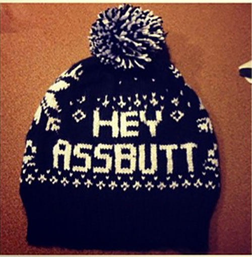 Knitted winter beanie hat with a pom-pom on top, decorated with white and black pattern and the phrase 'HEY ASSBUTT' in bold white letters.
