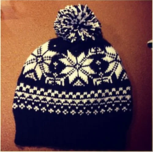 Black and white knit winter hat with a pom-pom, featuring snowflake and geometric patterns.