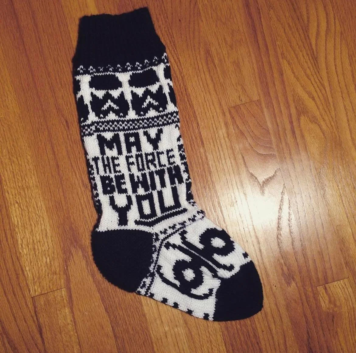 A black and white Christmas sock with Star Wars and Star Wars-themed design on a wooden floor.