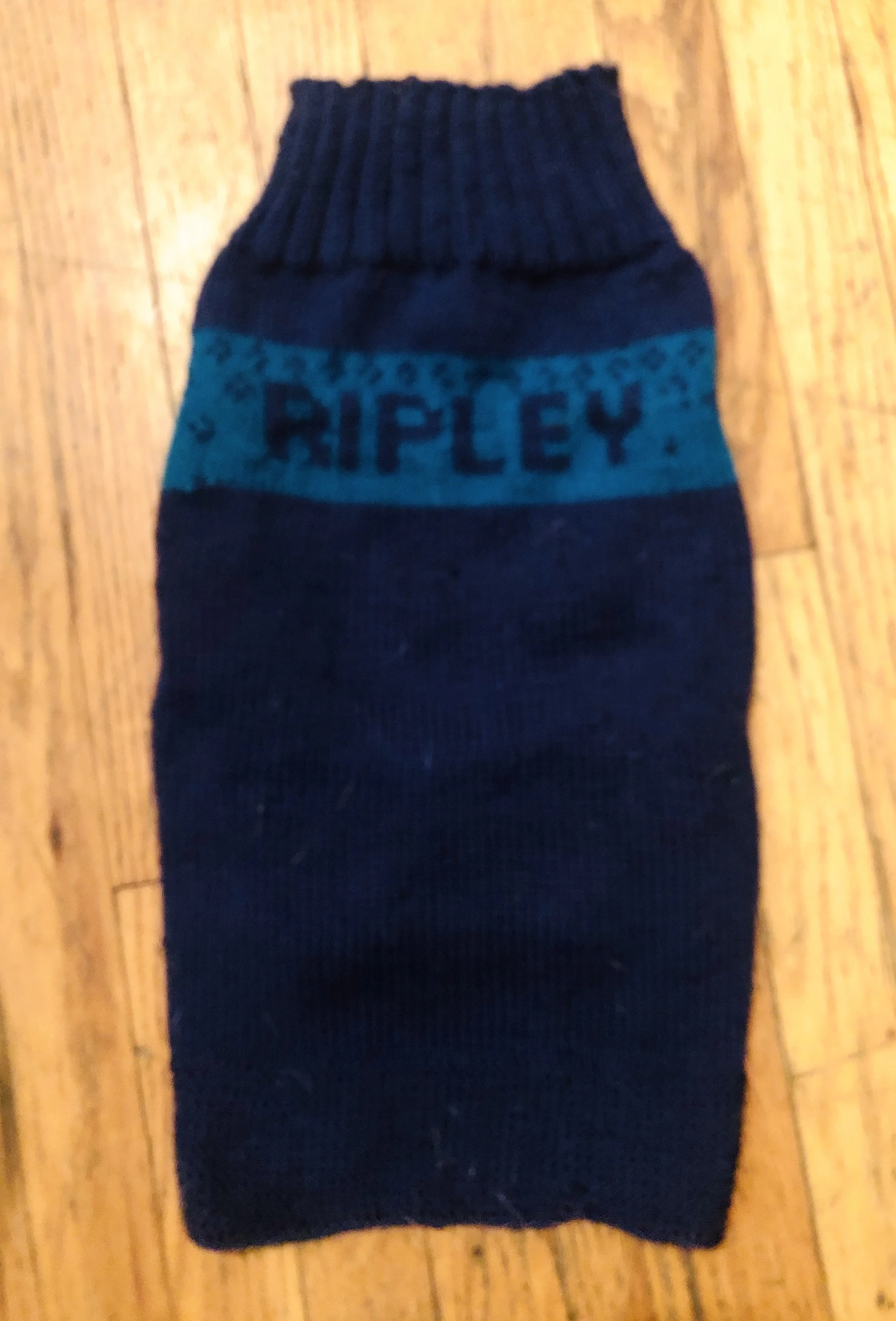 Black and blue knitted sock with the word 'RIPLEY' woven into the fabric, laid flat on a wooden surface.