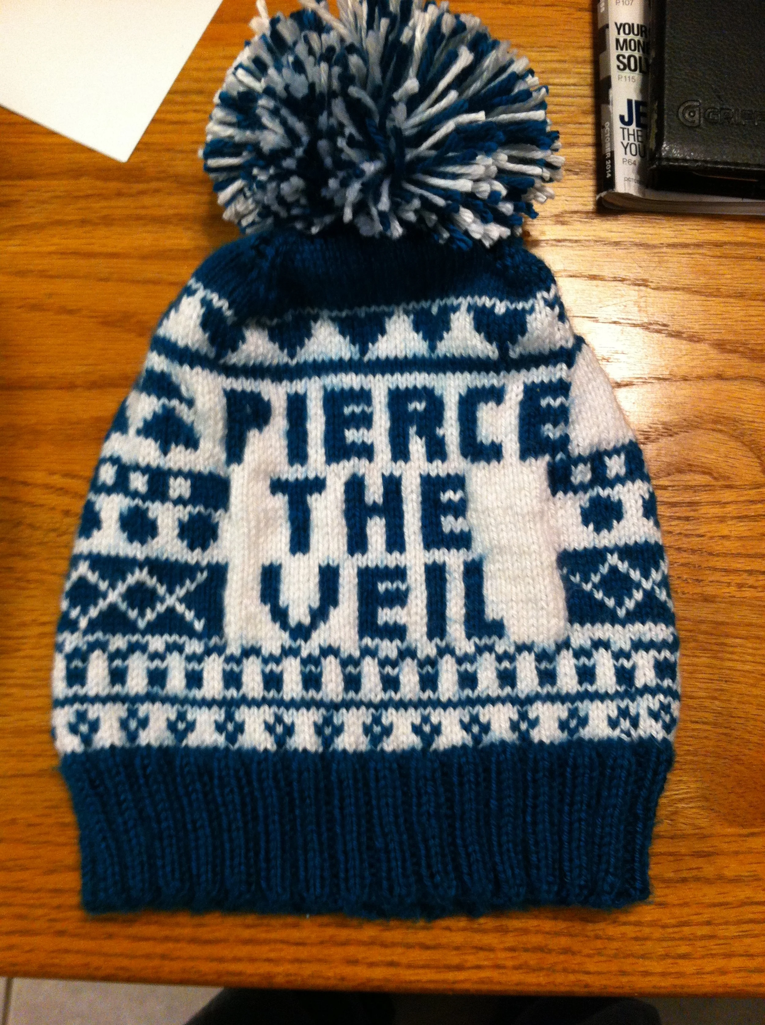 Close-up of a blue and white knitted winter hat with a pom-pom on top, resting on a wooden surface.