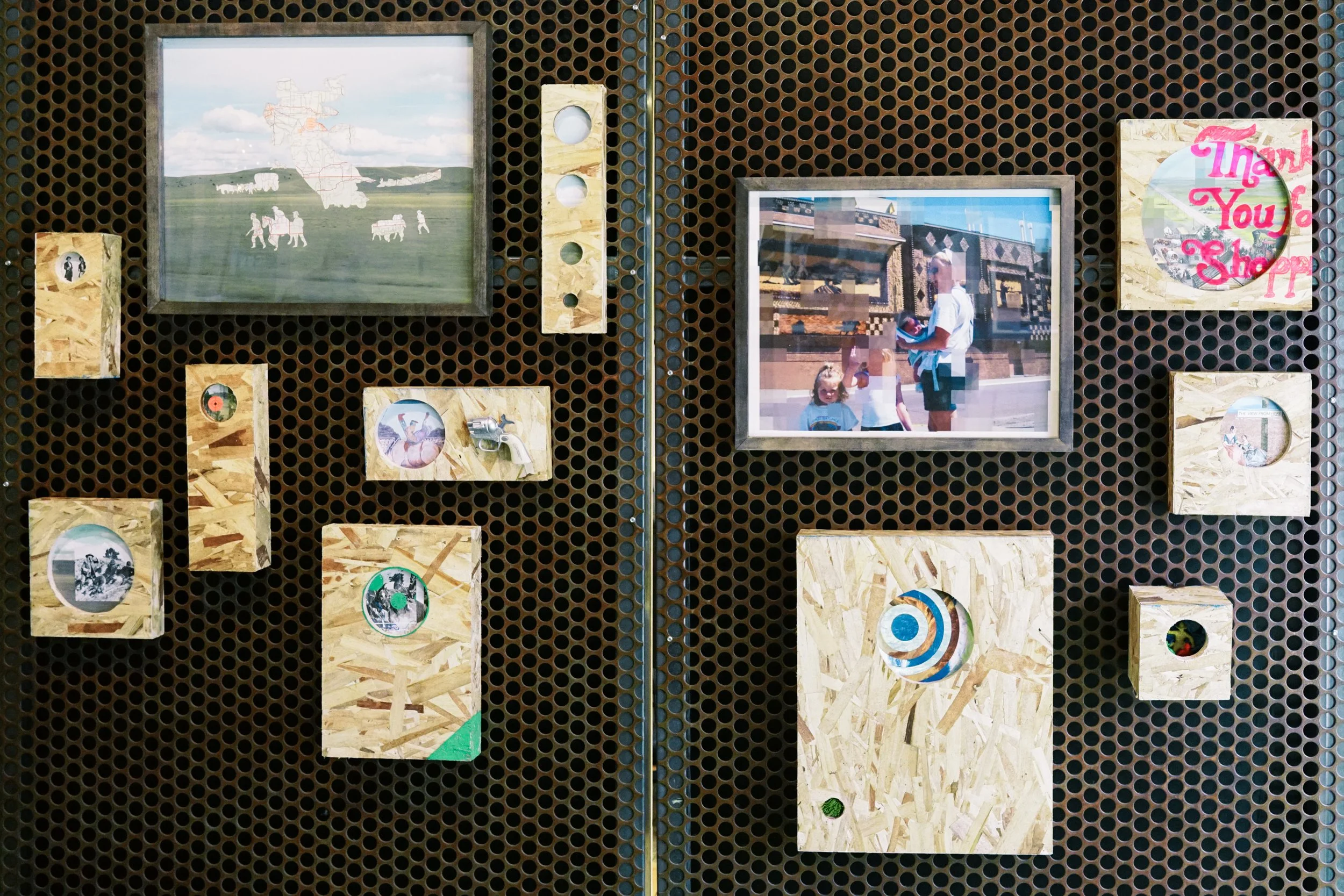 Display of various pictures and objects on a perforated black board. The images include historic towns, a scene with children and an adult, and a circular design with the words 'Thank You for Shopping' in pink. Some images are framed with wood and ot