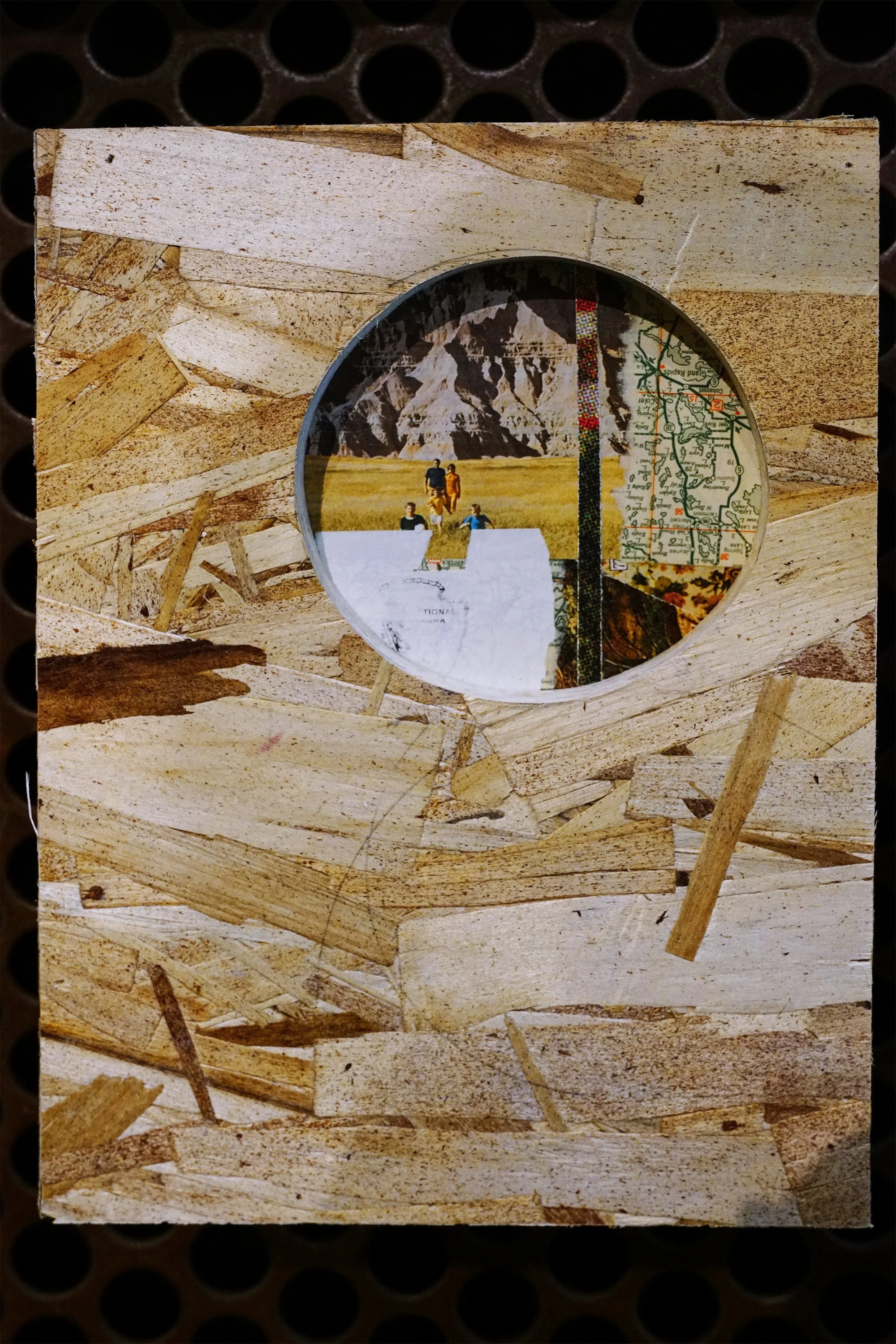 Round mirror reflecting a mountain landscape and people standing on a grassy field, framed by a rustic wooden wall.