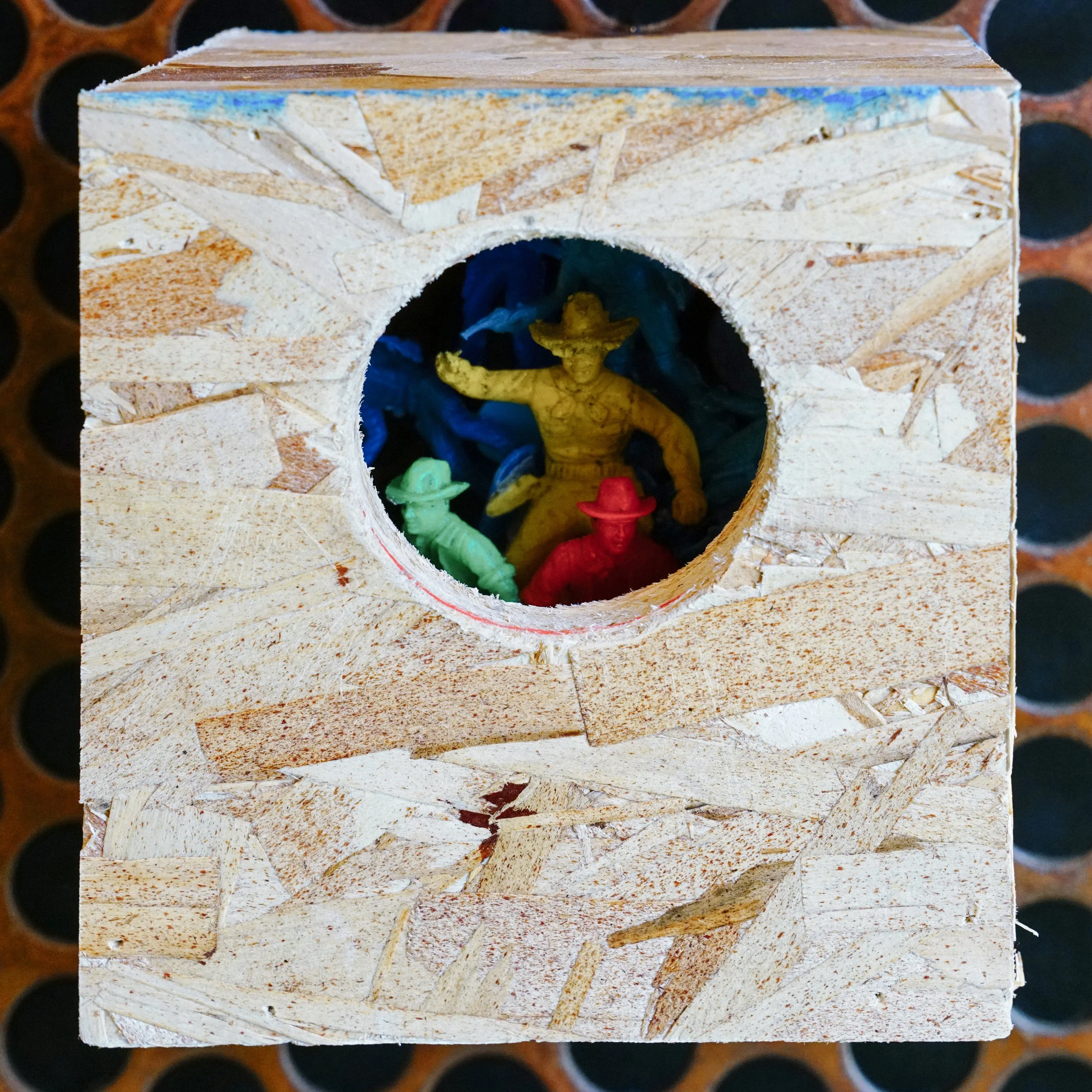 Close-up of a miniature figure of a person in a yellow outfit, placed inside a hollow, wood-textured structure with a circular opening.