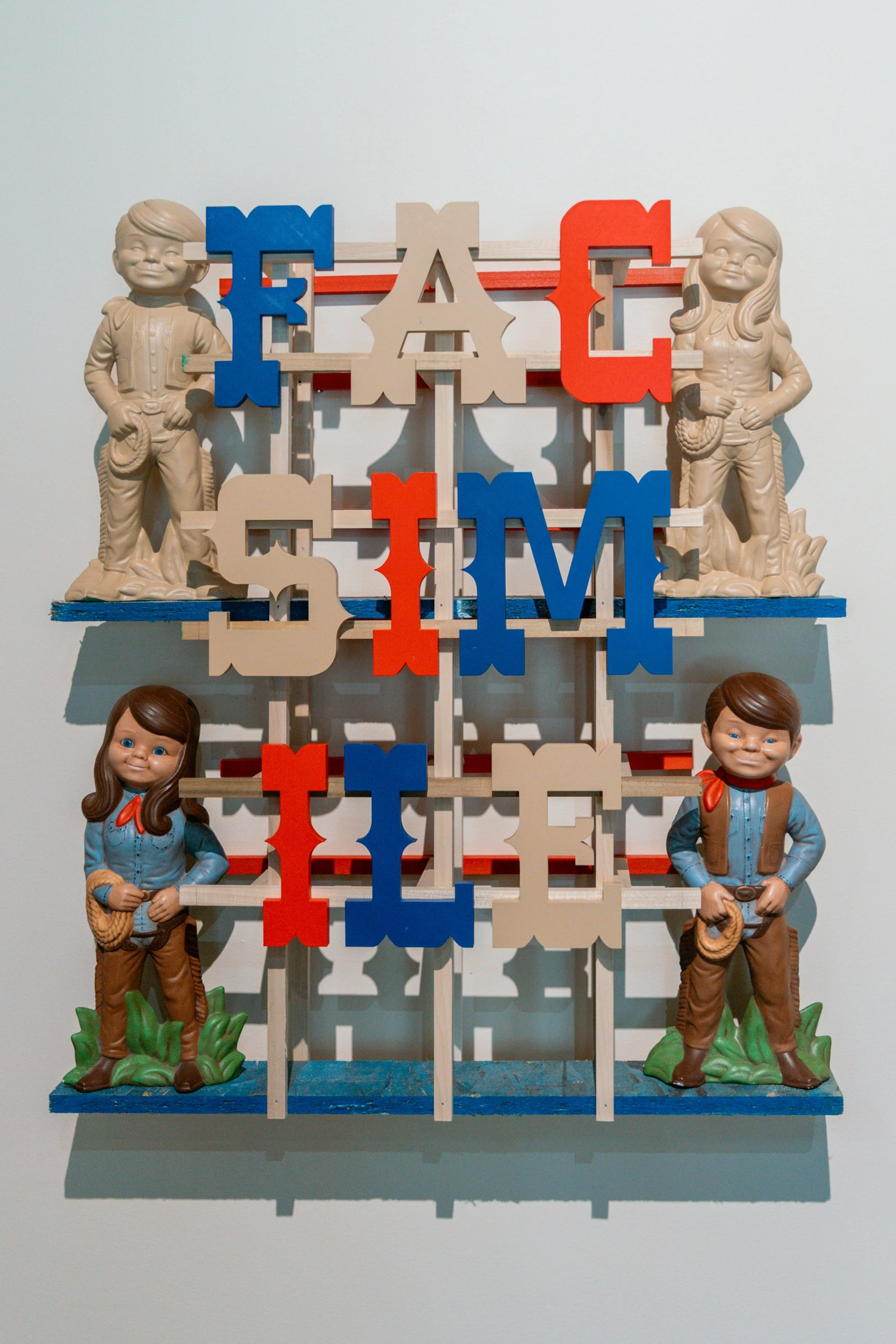 Wooden sculpture of children dressed as cowboys and cowgirls standing on a multi-leveled blue shelf, with colorful letters spelling 'FAMILY' in between.