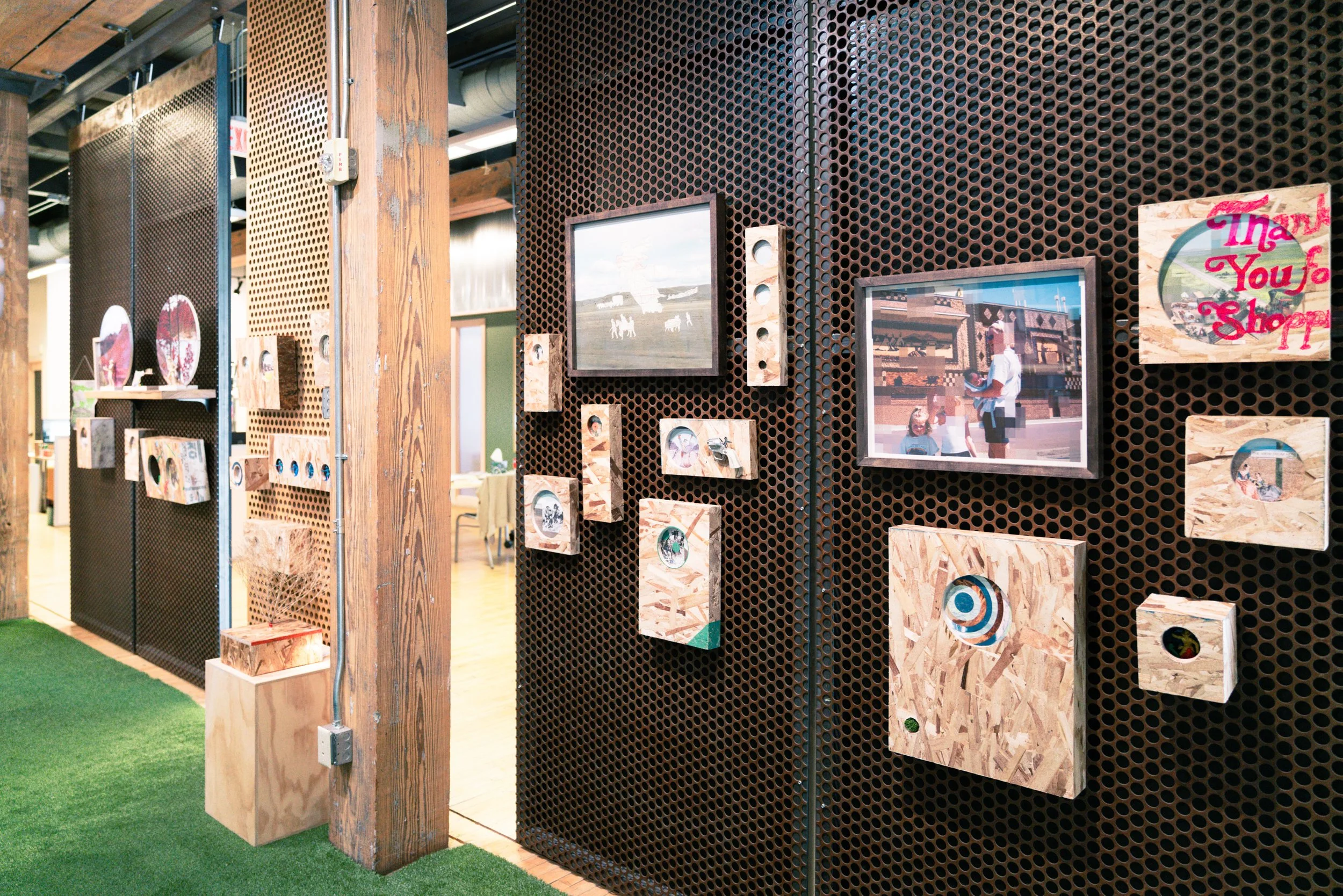 Interior view of a store display with framed photos on a perforated metal wall, wooden panels, and a sign that says 'Thank You for Shopping'.