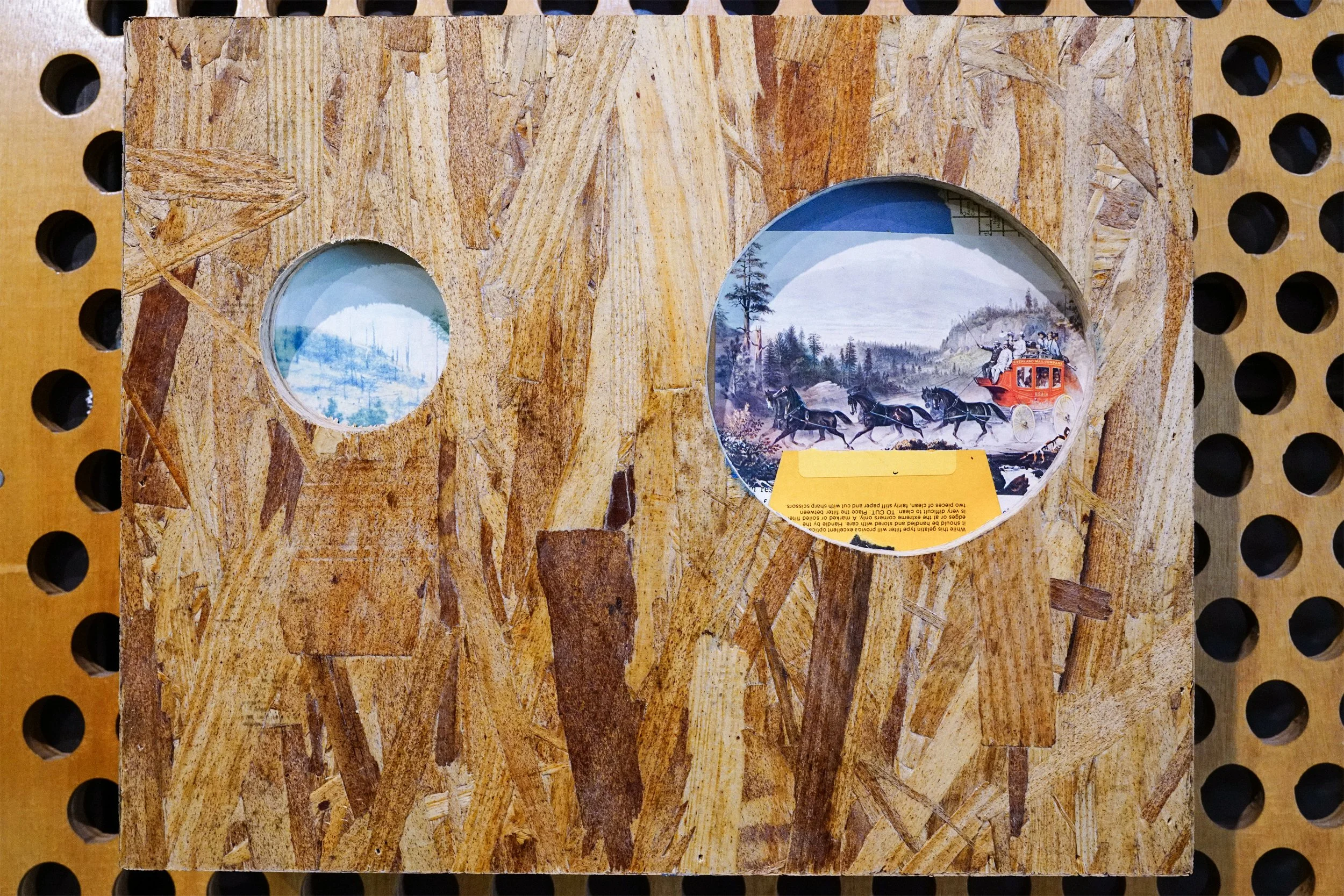 Wooden display case with two circular cutouts featuring scenic photographs, one showing a snowy landscape and the other a mountain scene with a horse-drawn carriage.