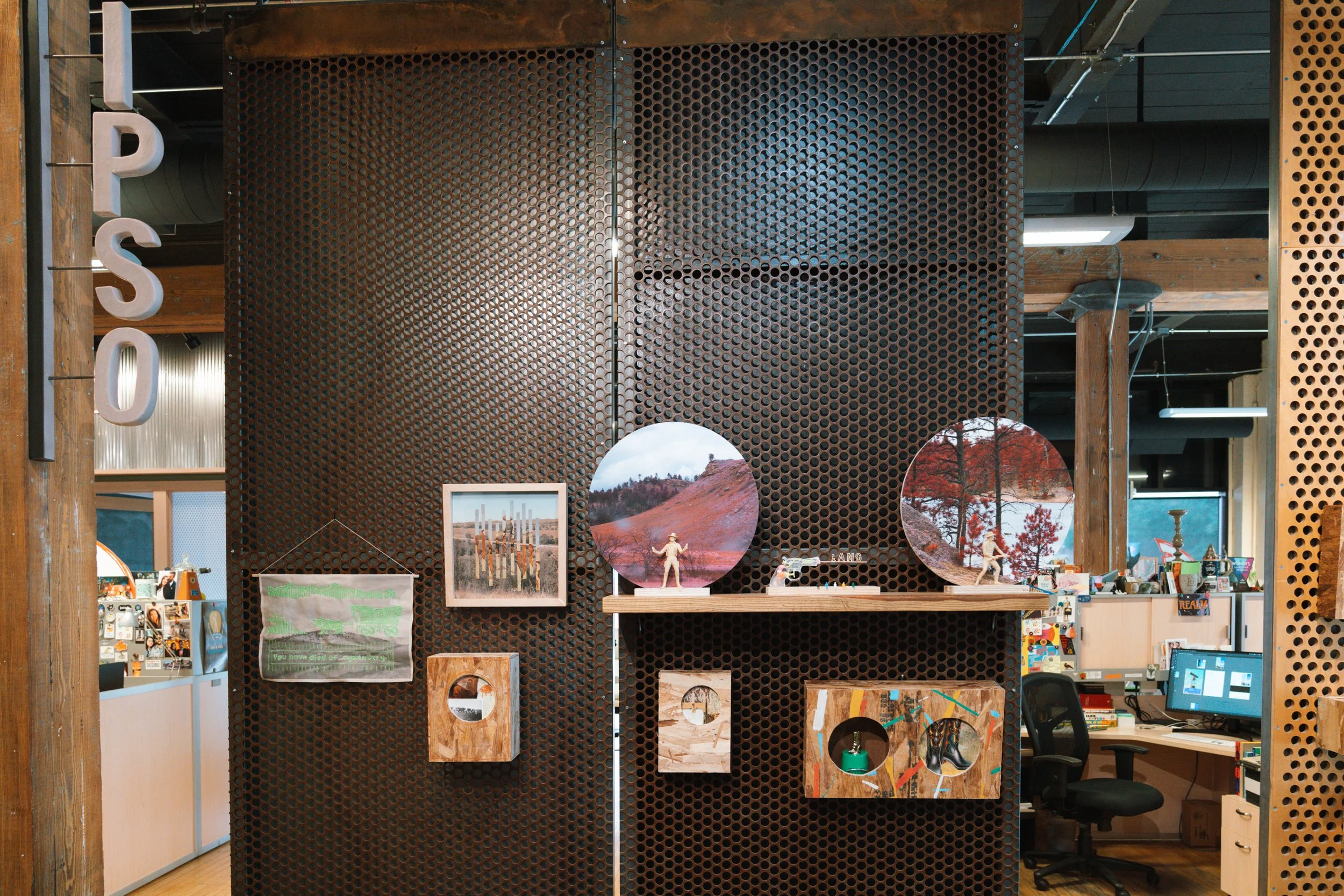 A wooden and metal display wall showing various landscape and art photographs, small sculptures, and decorative items in an indoor art or craft store.