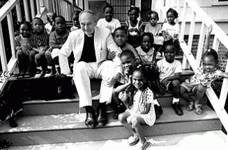 On the front steps of Emmaus House, Father Austin Ford and his dog, Cleopatra, visit with some of the children in the ministry’s pre-school (Photo by Ann Borde)