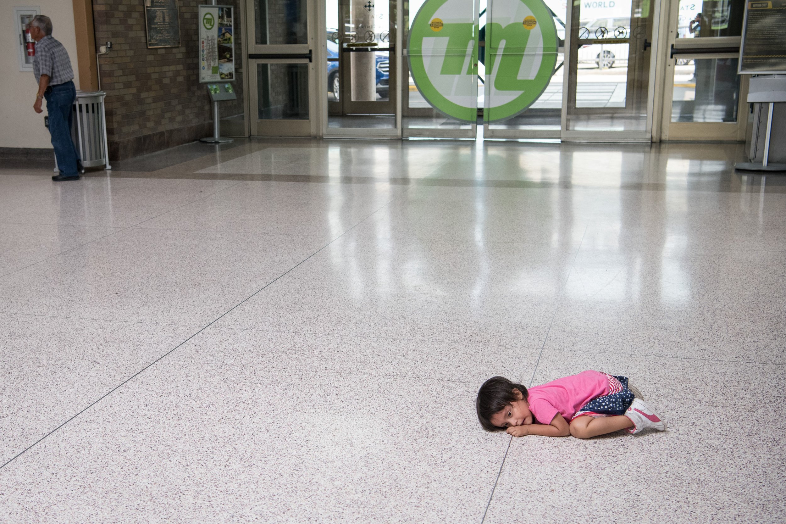  A young migrant girl sits on the floor as her father, recently released from federal detention with other Central American asylum seekers, gets a bus ticket at a bus depot on June 11, 2019, in McAllen, Texas. (Photo by LOREN ELLIOTT/AFP/Getty Images.) 