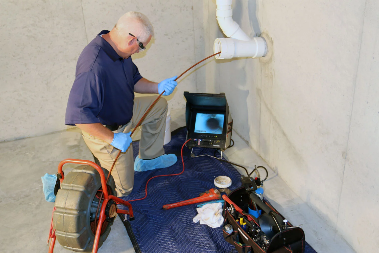Image of a man running a sewer camera snake trhough an access pipe