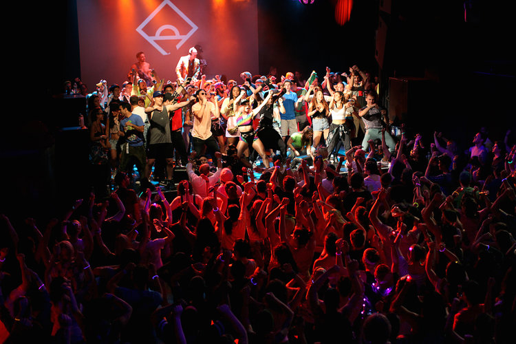 Irving Plaza is packed, wall-to-wall. Women in neon tank tops and guys in windbreakers sway and shake as Snap!'s '90s classic "The Power" blares from the speakers. "Heyyy! Ho! Heyyy! Ho," shouts a toned woman with pink hair and a spandex top, as she directs the room to break into the Butterfly and Sprinkler. "I'm seeing a lot of love!" yells a guy onstage, hyping up the mostly twentysomething crowd. Wearing a tight muscle t-shirt with his hat to the back, he's Marky Mark reincarnated. Welcome to Daybreaker. Founded by Radha Agrawal and Matt Brimer, the morning rave began in the city in 2013 as an alternative to obnoxious and elitist nightlife. "Over a late-night falafel in Williamsburg, we mused over an idea. An idea about dancing before the day broke with people we love. About cultivating a community that values wellness, camaraderie, self-expression, mindfulness… and mischief," the friends say. "At Daybreaker, we dance our faces off before work and feel gloriously healthy doing so." It's caught on. Daybreaker has expanded to 11 cities, with events across the country as well as in Paris and London. So what's a morning rave really like? Well, first off, it's early. For a night owl like me, getting up was the hardest part. I set my alarm clock for 6:00am for a May event (and 6:10am and 6:15am, just to make sure I really woke up). Daybreakers can start as early as 7:00am. Okay, I'm here. At a regular nightclub, now would be the time to head to the bar or--if I'm lucky--someone's getting me a drink. Not here. Daybreaker is completely alcohol and drug free. No wake and bake, kiddos. However, they do serve water and healthy juices. I help myself to an organic coconut water and settle for a spot near the rear of the room. Partygoers are mostly women and from the looks of it, and a lot of people have come in groups. Friends, coworkers and one couple who can't stop making out while a Prince song plays. Some committed to dressing along the '90s party theme--think fannypacks and retro shirts--while others are wearing their work clothes. The energy is kept high with spontaneous "moments" like live horns, drummers and professional dancers. The best part about Daybreaker is ther are no rules. Dance, pump up your cardio or stand creepily in the corner (like me). It's all good. Everyone vibes to the music and there's zero judgement. Unlike every other party, no one is distracted trying to look cool or take selfies. In fact, I don't see one, single cell phone out. “We often live routine lives. It’s a wink to your day,” Radha says about Daybreaker. “It’s a place where you can get loose and let your freak flag fly.” Around 9:00am, the freaks start to disperse from the dance floor. It's time to get to work, school and whatever routine--until the next one. A girl in front of me slings her backpack on her shoulder as we walk out. "This was so awesome," she says to her friend, wiping sweat from her face. "I really needed this." Get your tickets to Daybreaker here. Source: http://www.oxygen.com/very-real/what-its-like-to-go-to-an-early-morning-totally-sober-rave