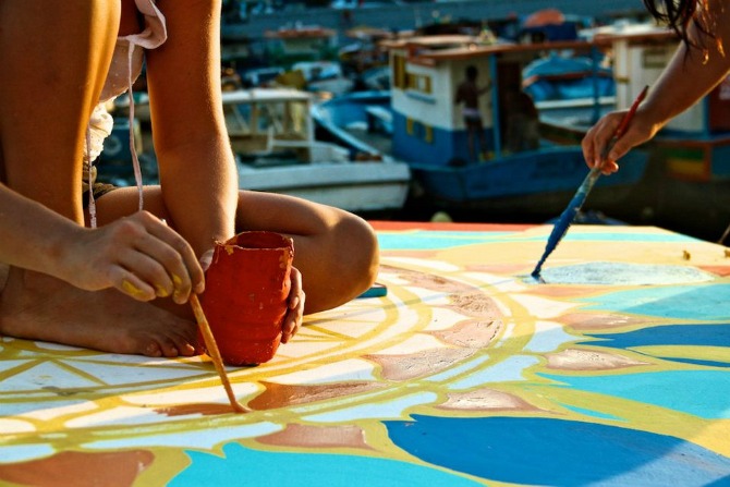   Maxine and co creator  Nicolina  painting a mural on a boat rooftop     In 2012, Maxine co-created  FlutuArte , a public art installation where 45 international artists joined to paint murals on the rooftops of 60 fishing boats in a historic harbor