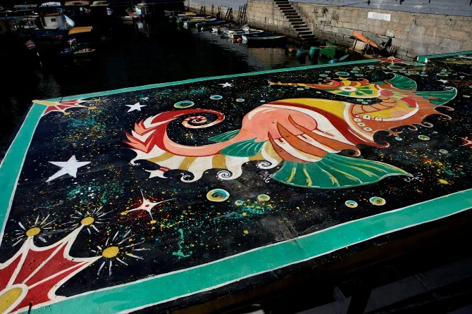 Seahorse mural by Maxine Nienow In 2012, Maxine co-created FlutuArte , a public art installation where 45 international artists joined to paint murals on the rooftops of 60 fishing boats in a historic harbor in Rio de Janeiro, Brazil. FlutuArte brought not only new vibrant colors to this fishing community, but also a new economy of tourism.