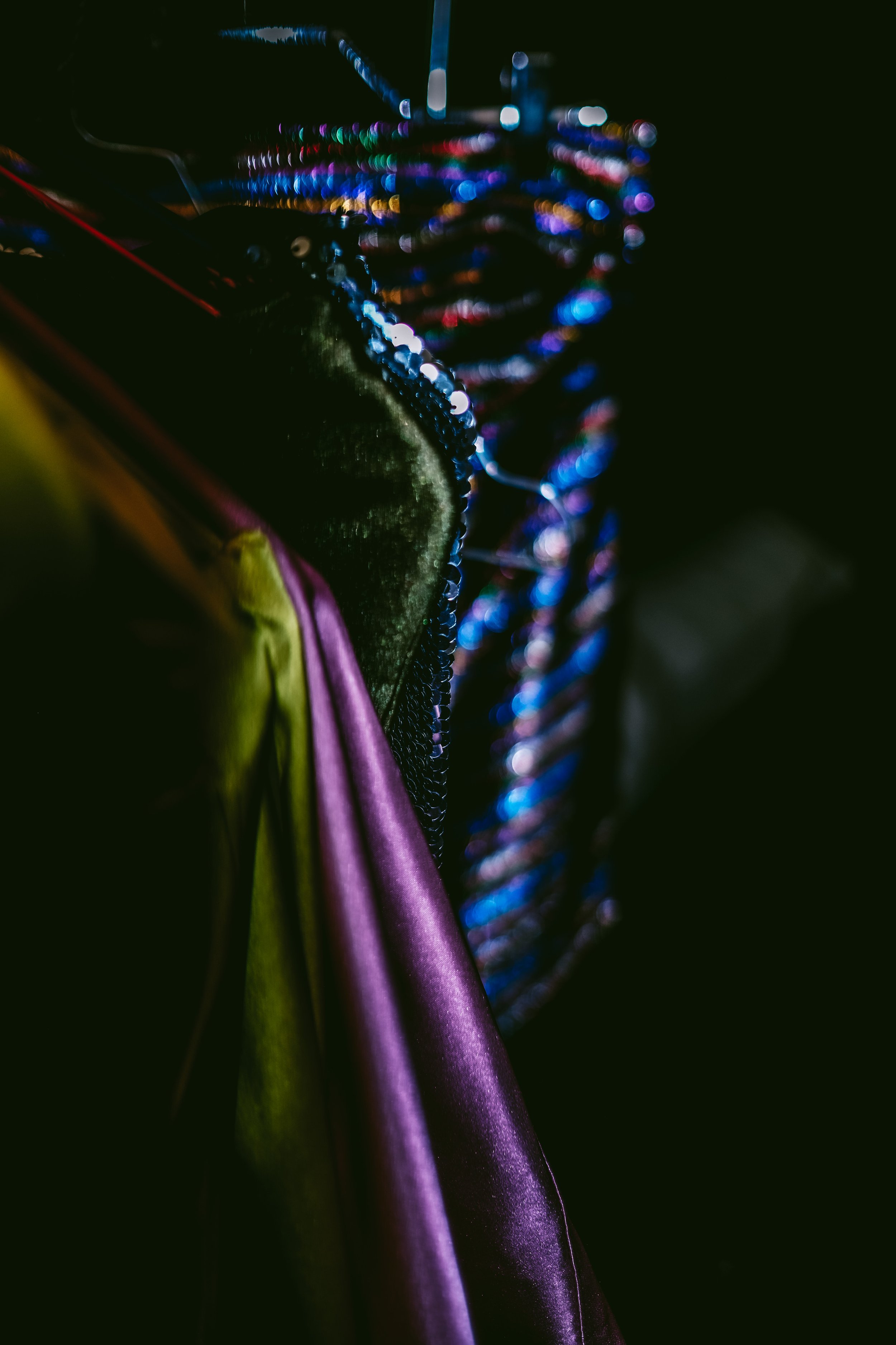 Close-up of colorful sequined textile fabric with reflections and a purple satin ribbon in a dark setting.