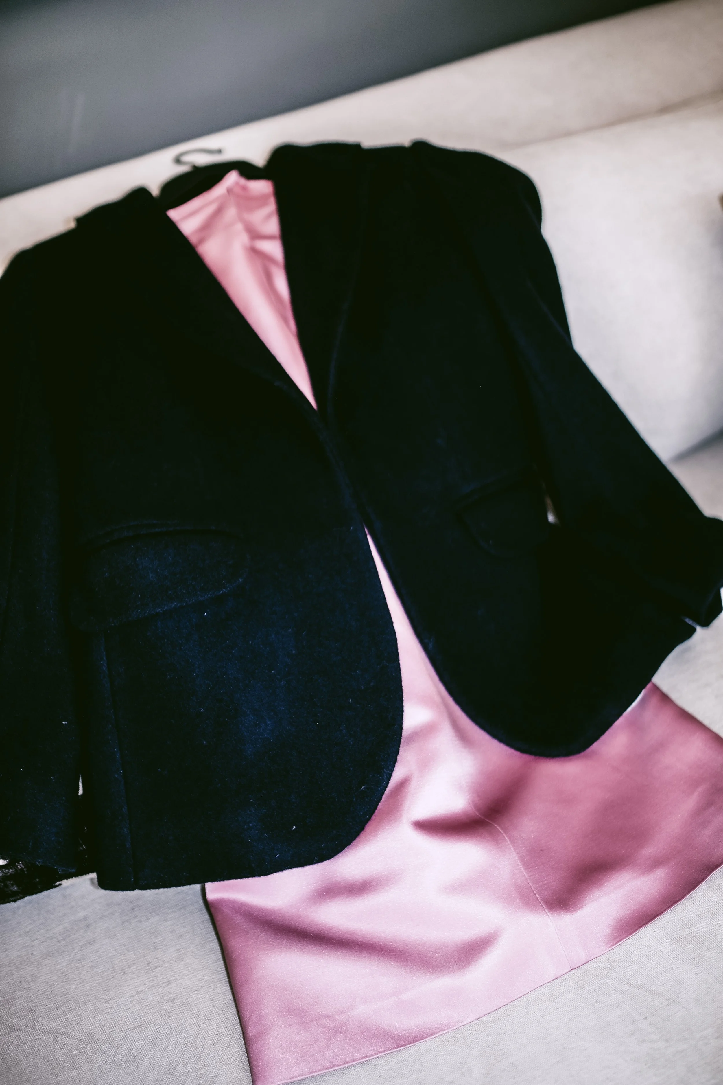 Black jacket with pink satin lining draped over a beige armchair.