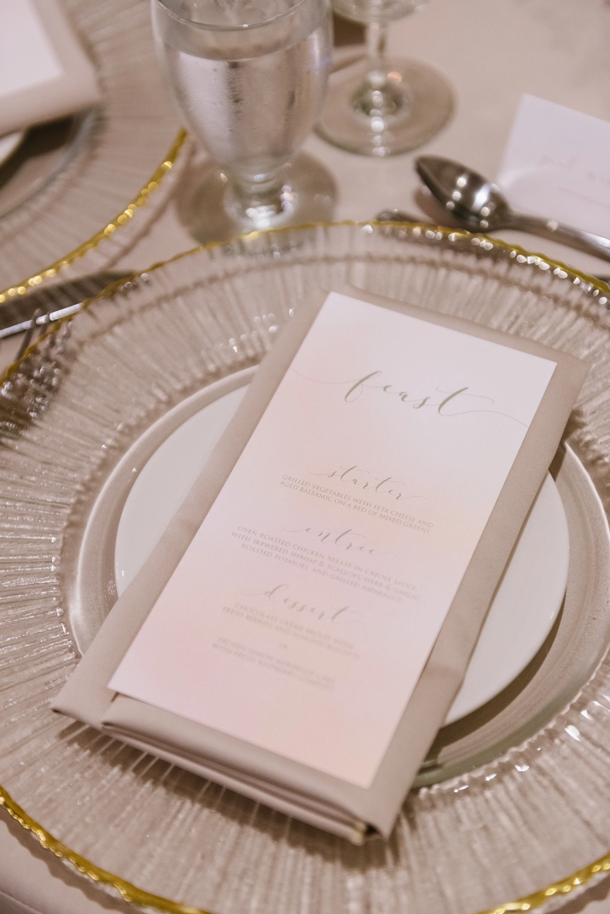 Calligraphy menu cards printed on a soft watercolour background, and placed on glass metallic-trimmed charger plates, mixes the refined with the undone. Venue: St. Marys Golf & Country Club.