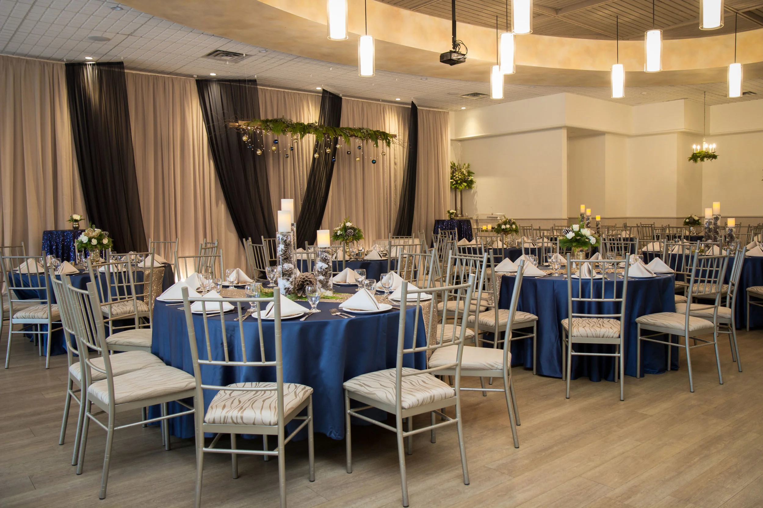 Rich navy blue linen, suspended winter greens, and flickering candlelight add an intimate holiday feel to a winter wedding setup. Venue: St. Marys Golf & Country Club . Decor & Styling: Above & Beyond Event Design . Floral Design: Lyric Flowers . Photography: David Jordan Photography.
