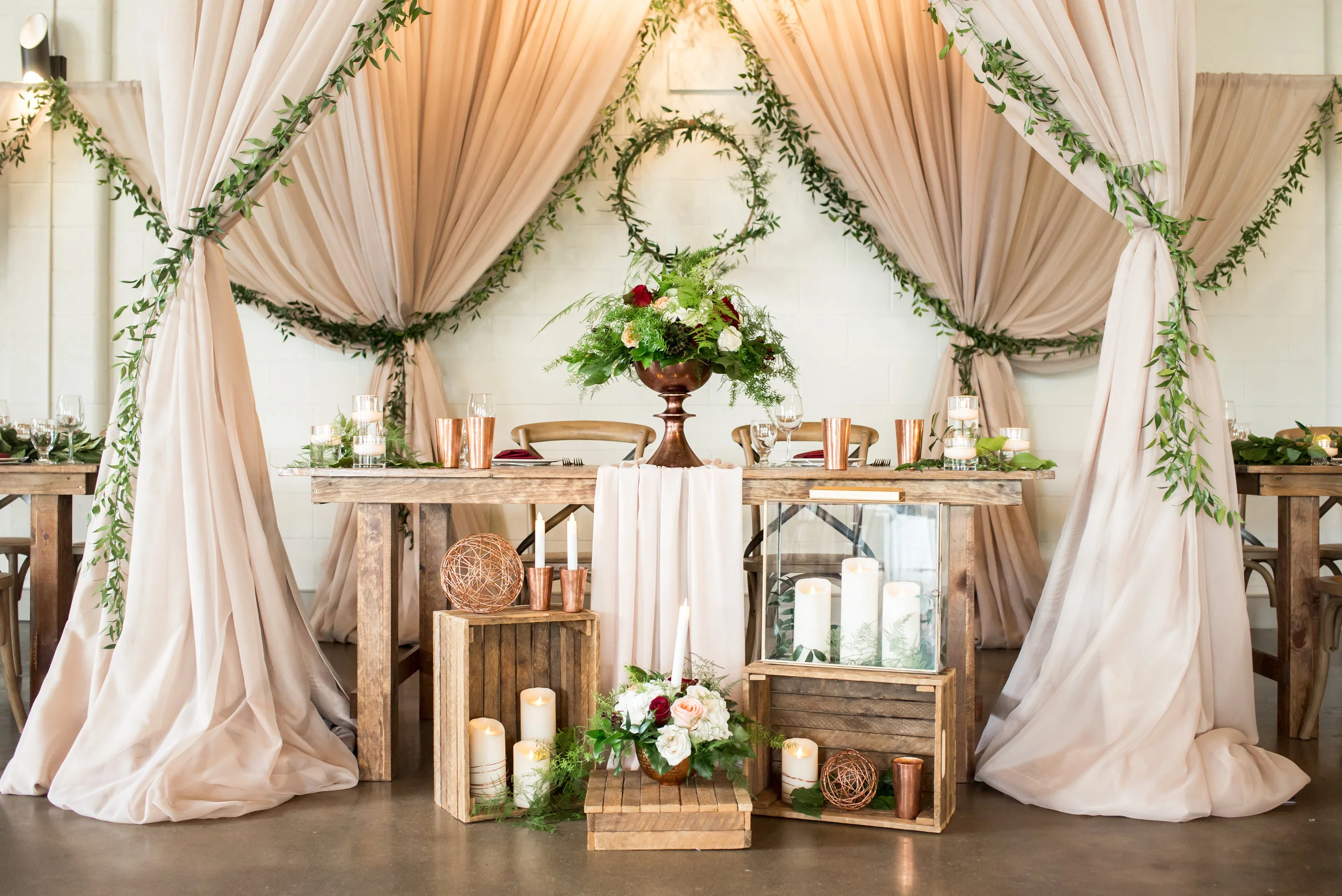 An intimate sweetheart table was set beneath the chuppah at the center of the Hideaway design, with romantic accents like a flowing chiffon runner, greenery wreath and garland, and a multitude of candlelight.