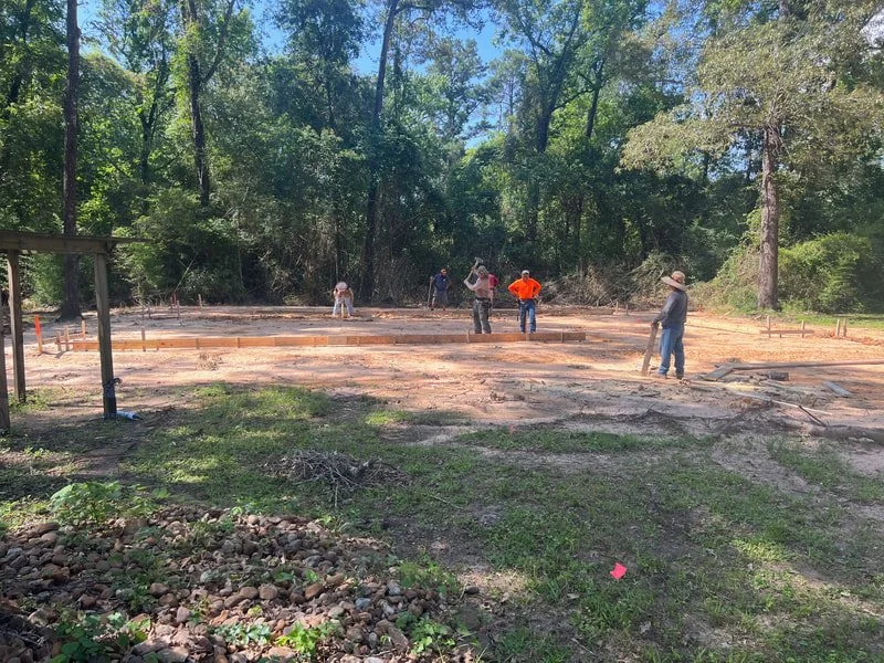Construction workers laying the foundation for a building in a forested area.