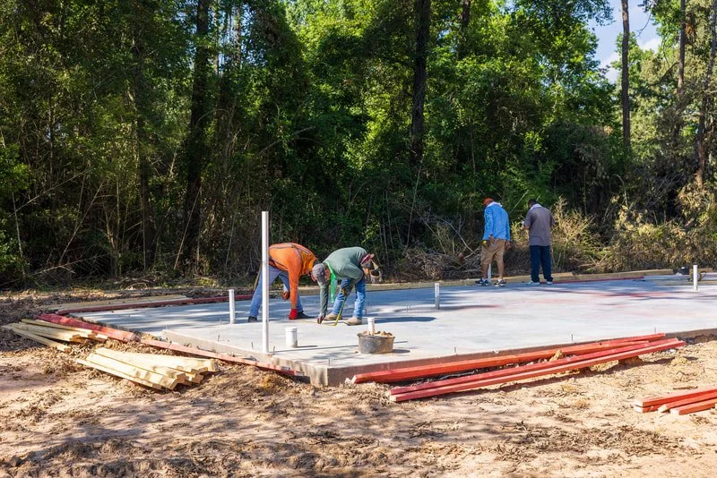 Four workers laying concrete on a construction site in a wooded area.