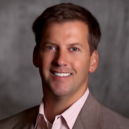 Professional portrait of a smiling man in a suit with a gray background.
