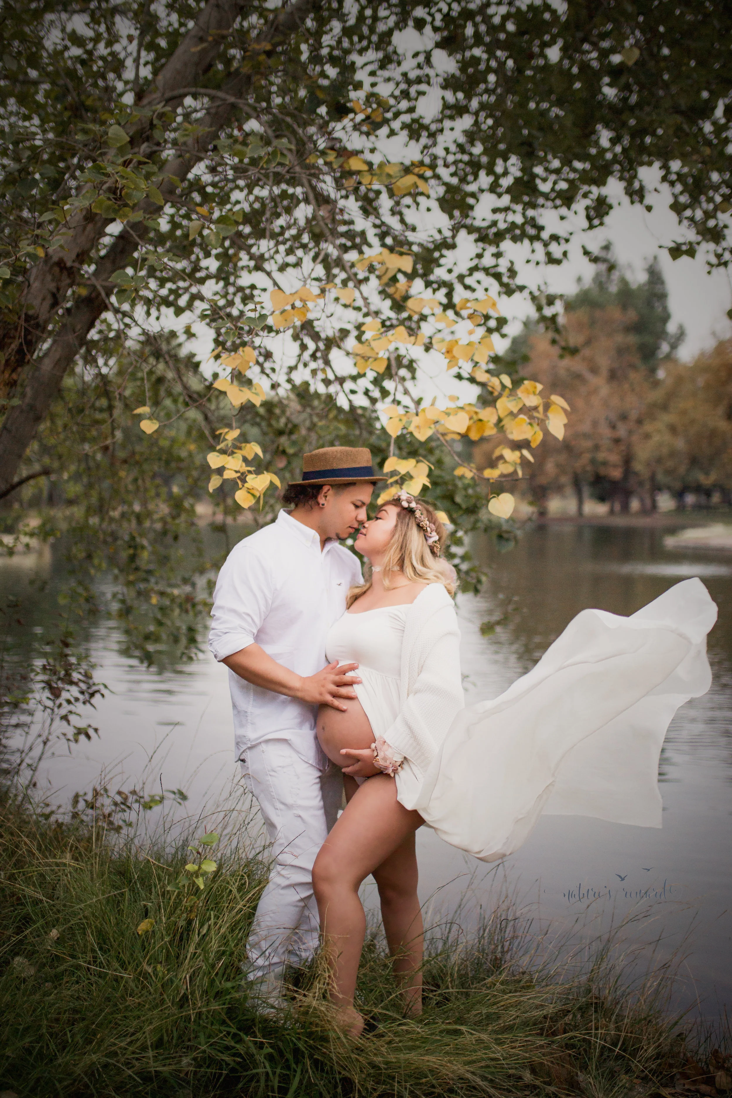The kiss and the dress in the wind by a beautiful lake under golden leaves in this loving and touching maternity portrait