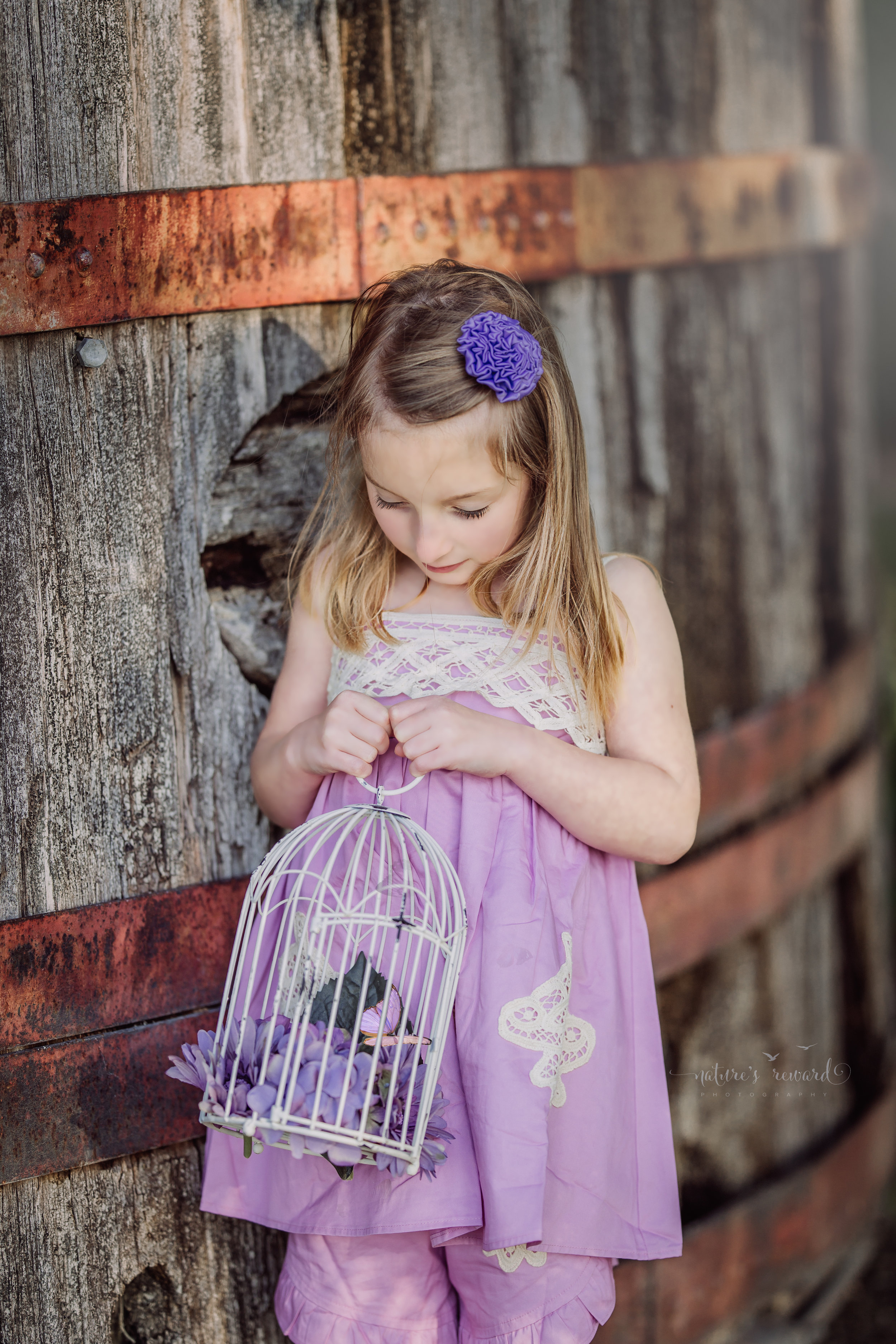 Young girl in a purple dress holding a bird cage with one sweet purple butterfly in it. Her eyelashes and sweet lips are the center of attention in this detail portrait