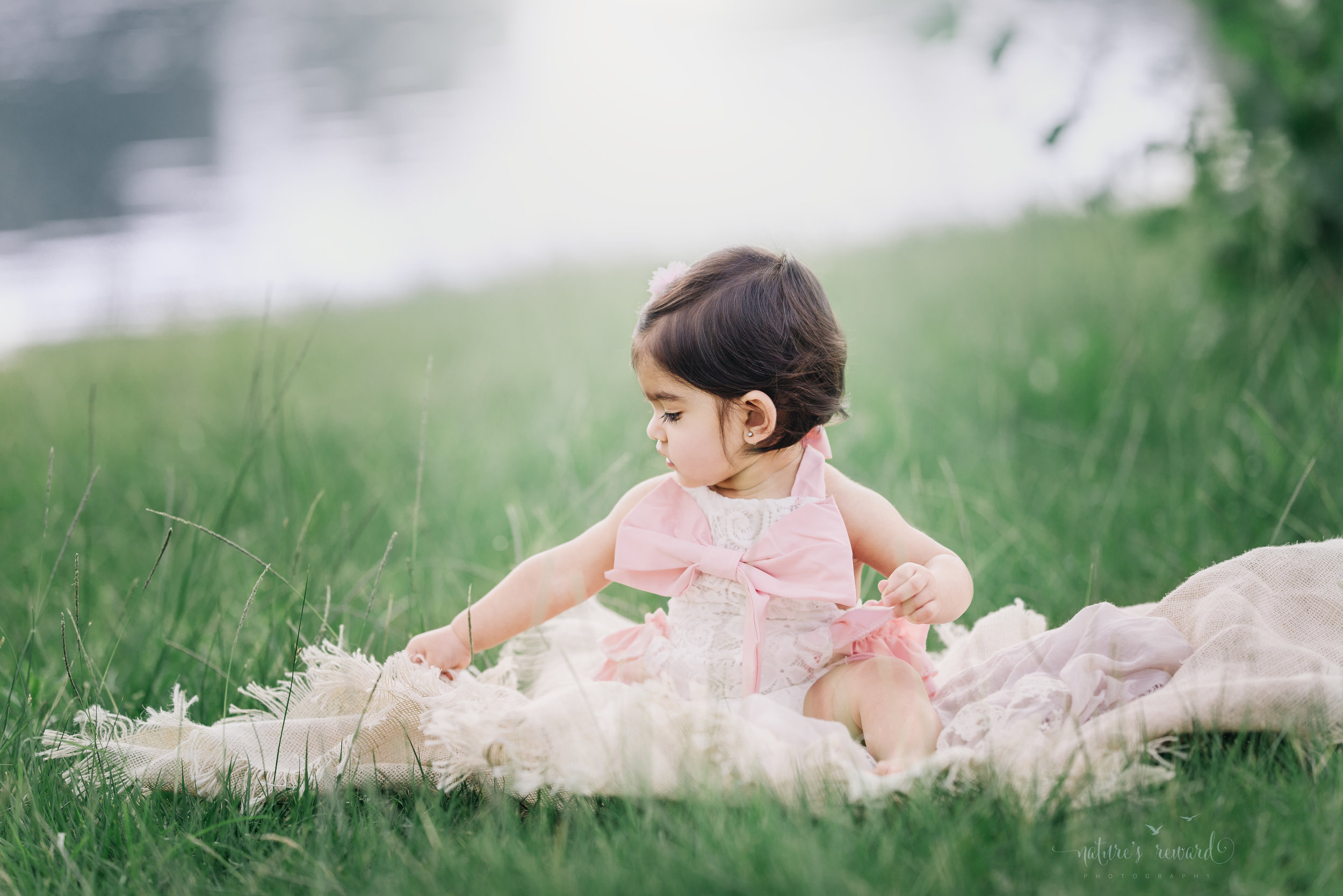 Magic by the water. Lovely little girl sits next to the lake in this summer portrait.
