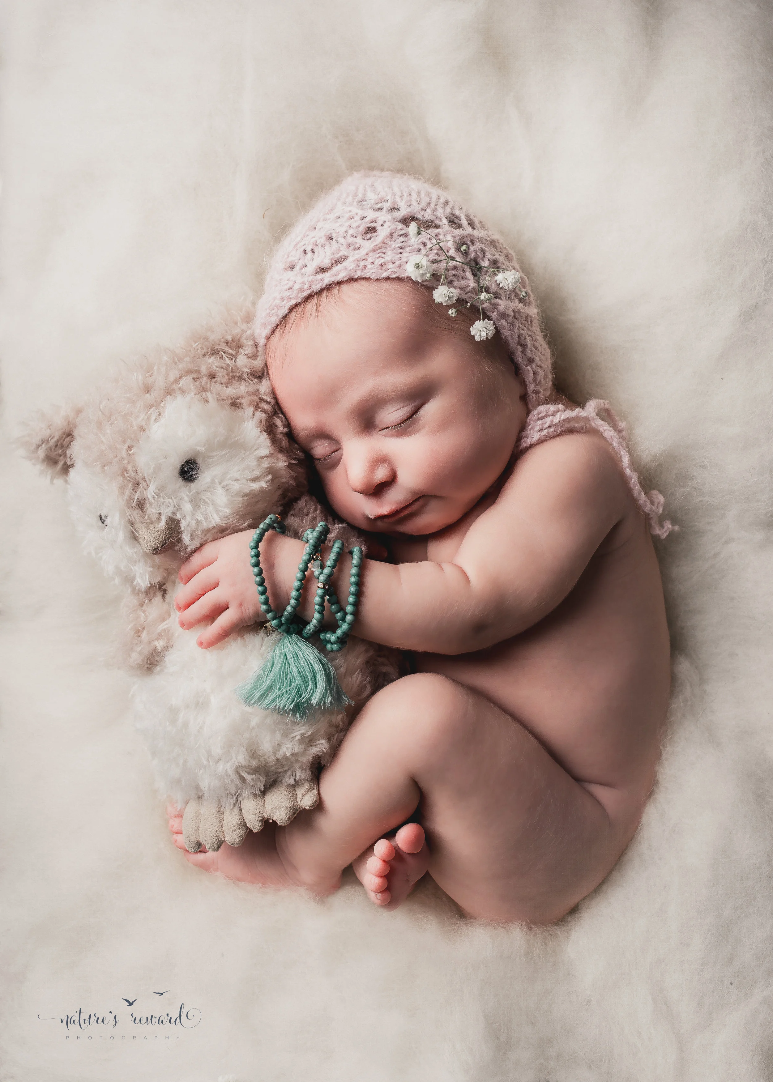 Newborn baby portrait in whites and soft pink, laying on a doll bed holding her owl. A Portrait By Nature's Reward Photography, a San Bernardino Family, Child, and Newborn Baby Photographer. 