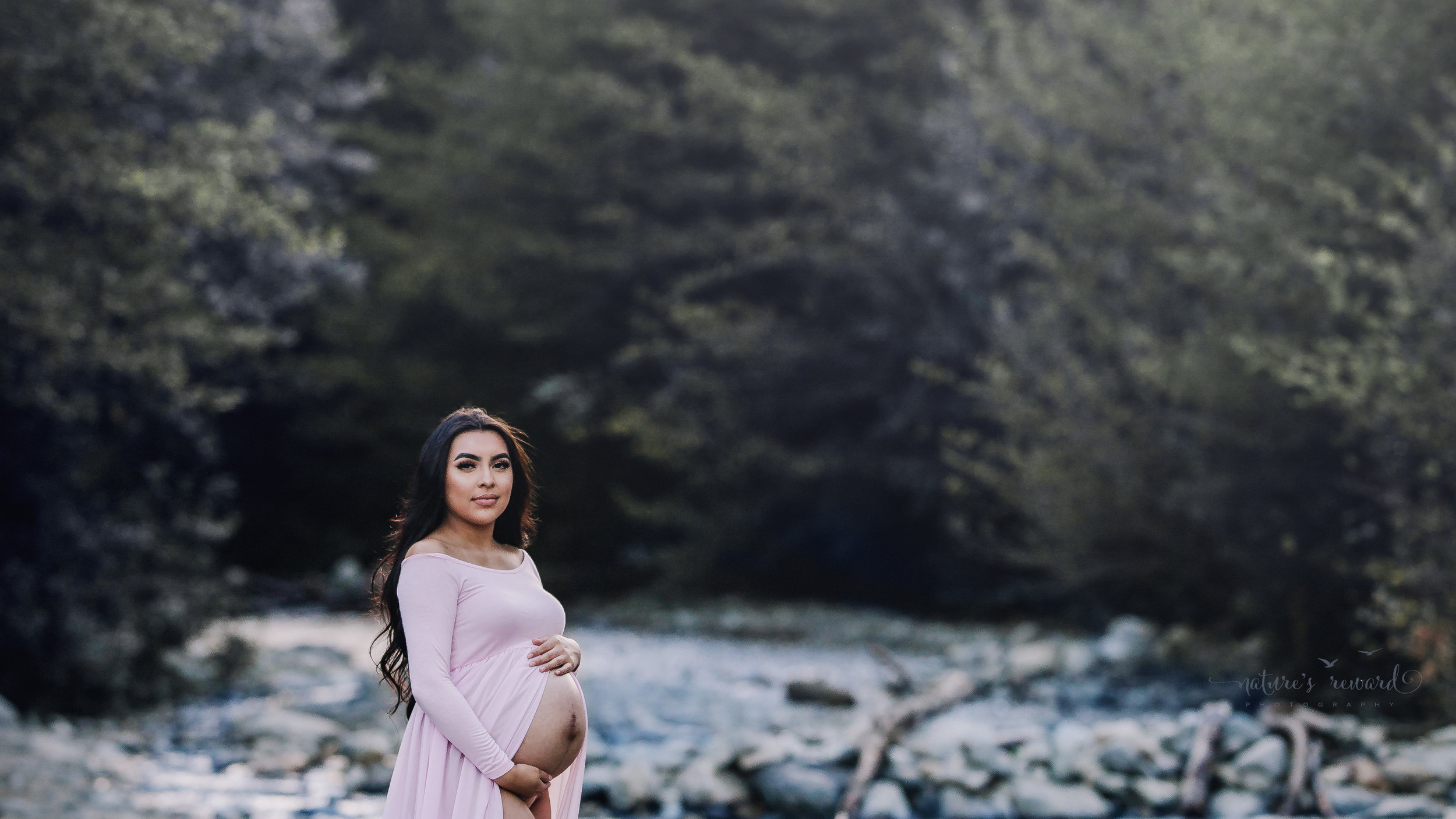 Gorgeous expecting mother in a pink maternity gown by the creek on a hot summer’s day