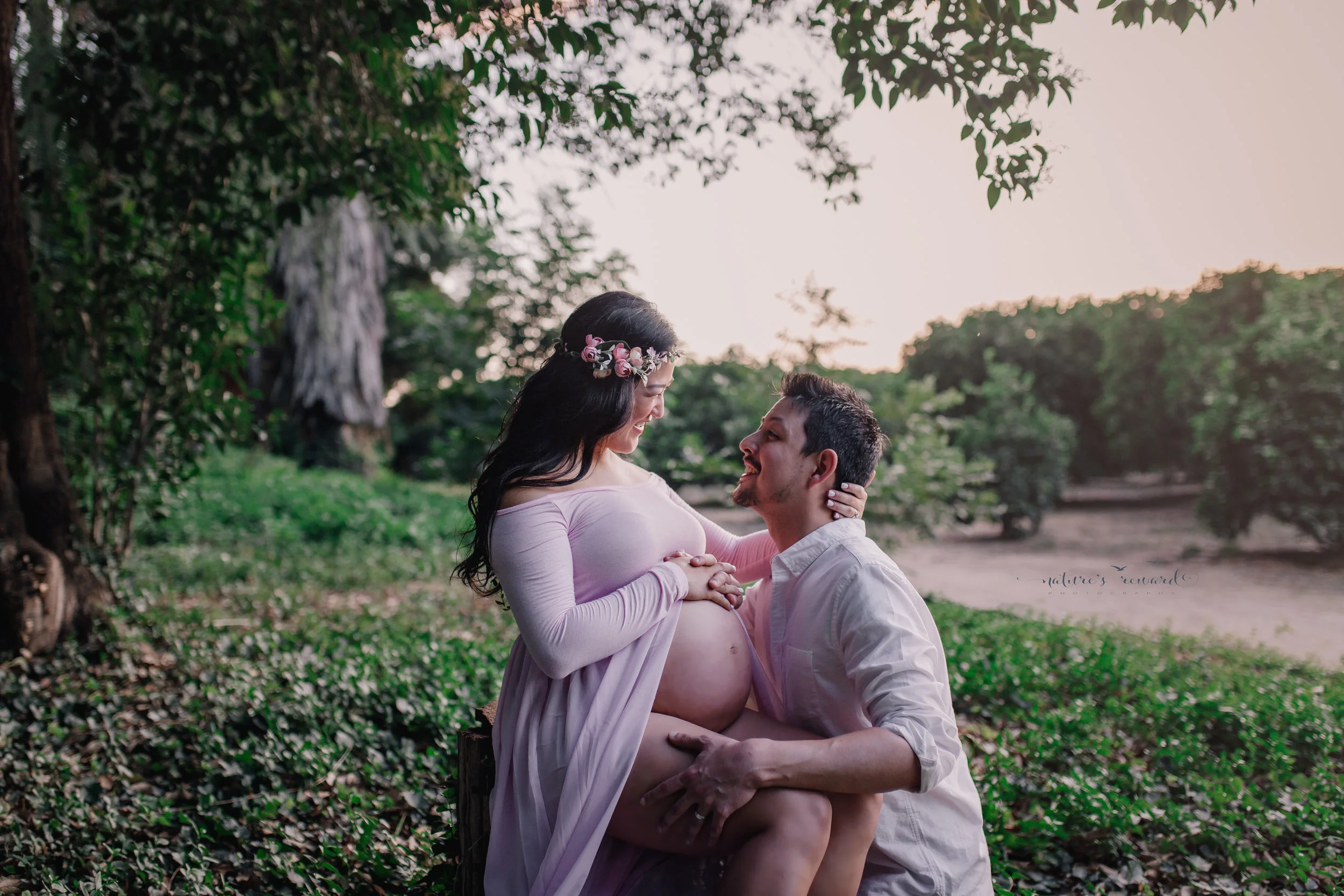 Gorgeous expecting mother in an open front gown gown smiles happily at the father of her unborn baby in this gorgeous maternity session portrait