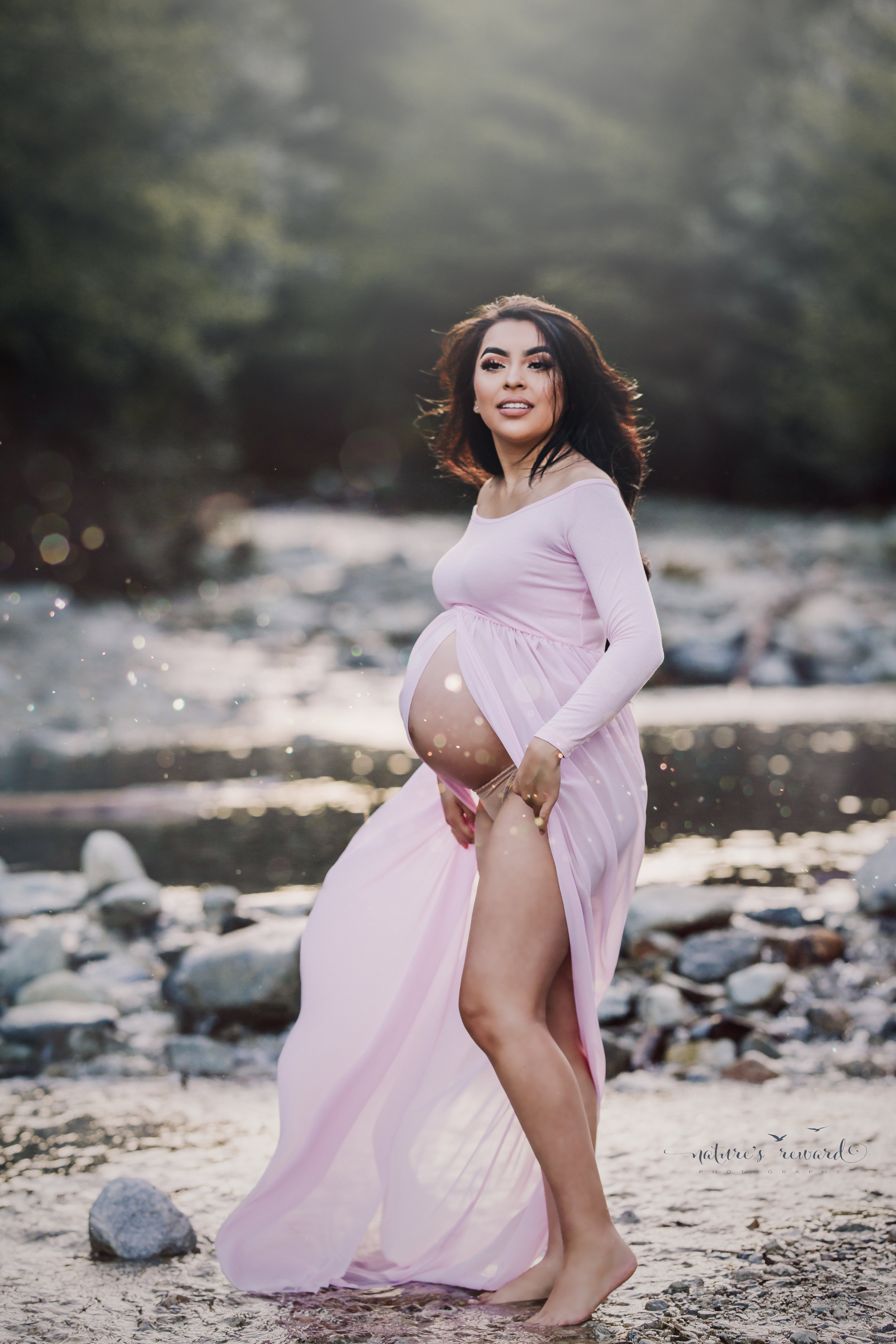 Gorgeous Mother to be gets ready to pose in this spectacular candid maternity session portrait in a pink open front gown in a stunning creek location.