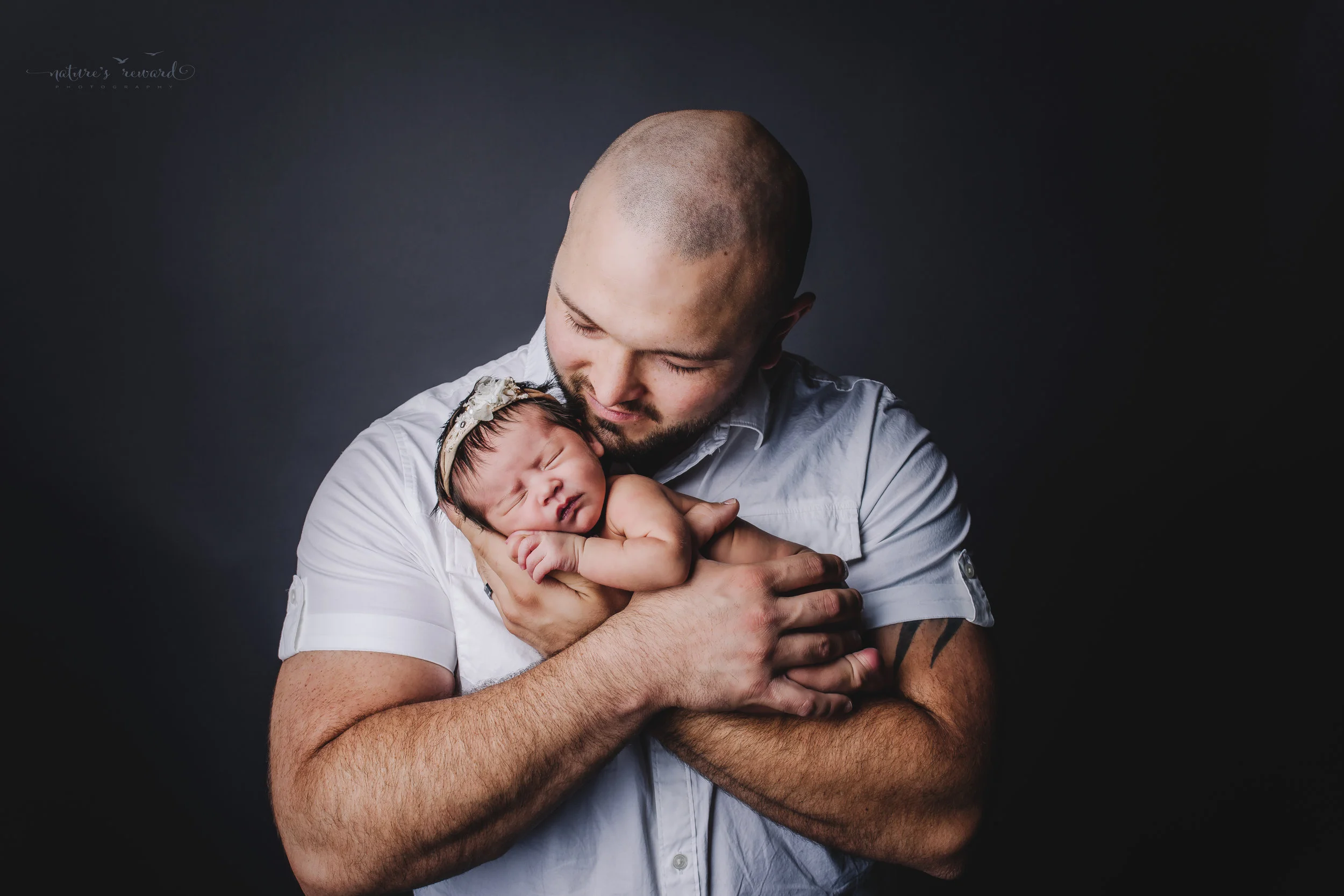 Father holding his newborn baby girl in his arms. A portrait by Nature’s Reward Photography