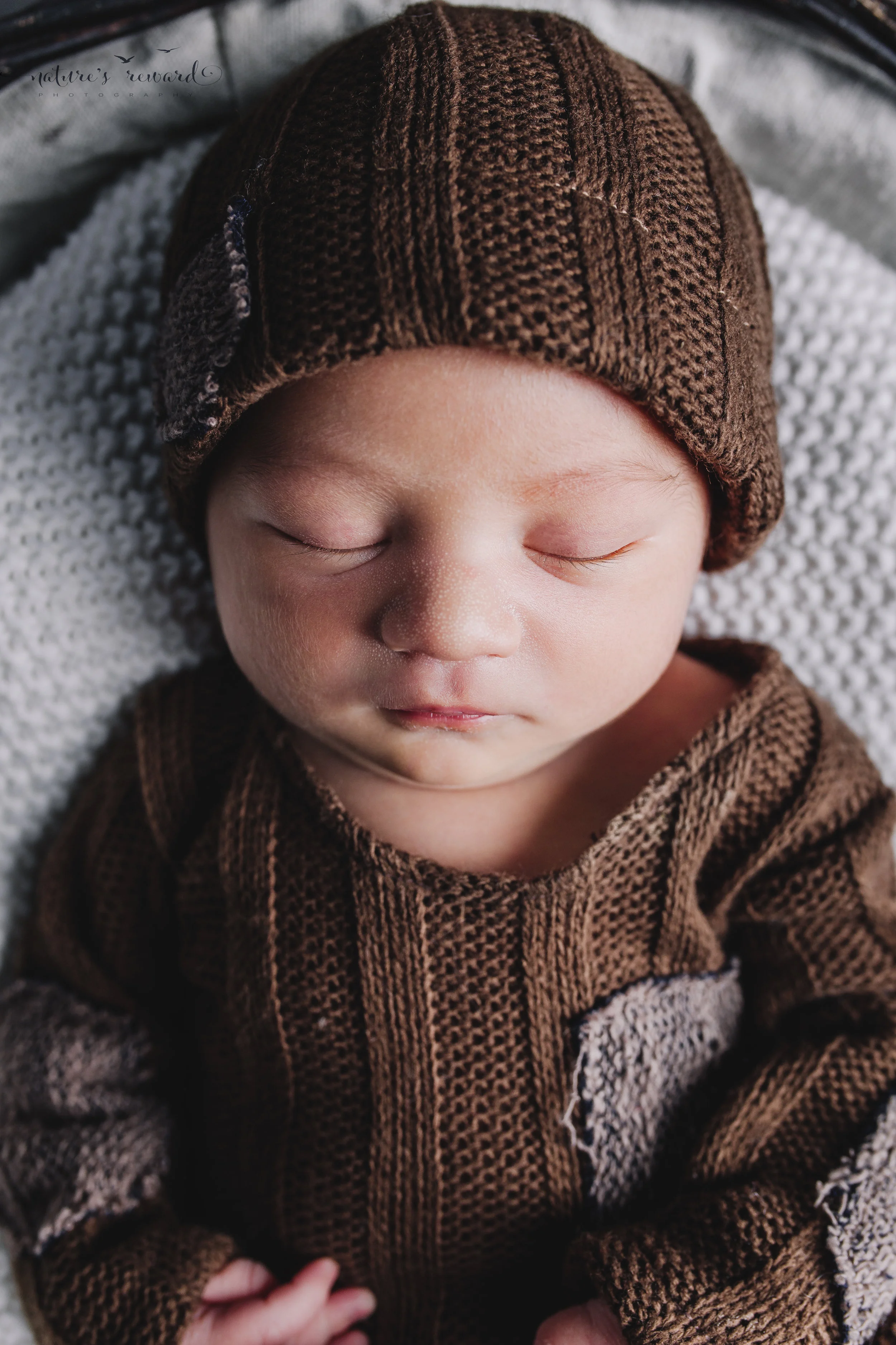 Newborn baby boy portrait wearing a brown outfit and matching cap by Nature’s Reward Photography
