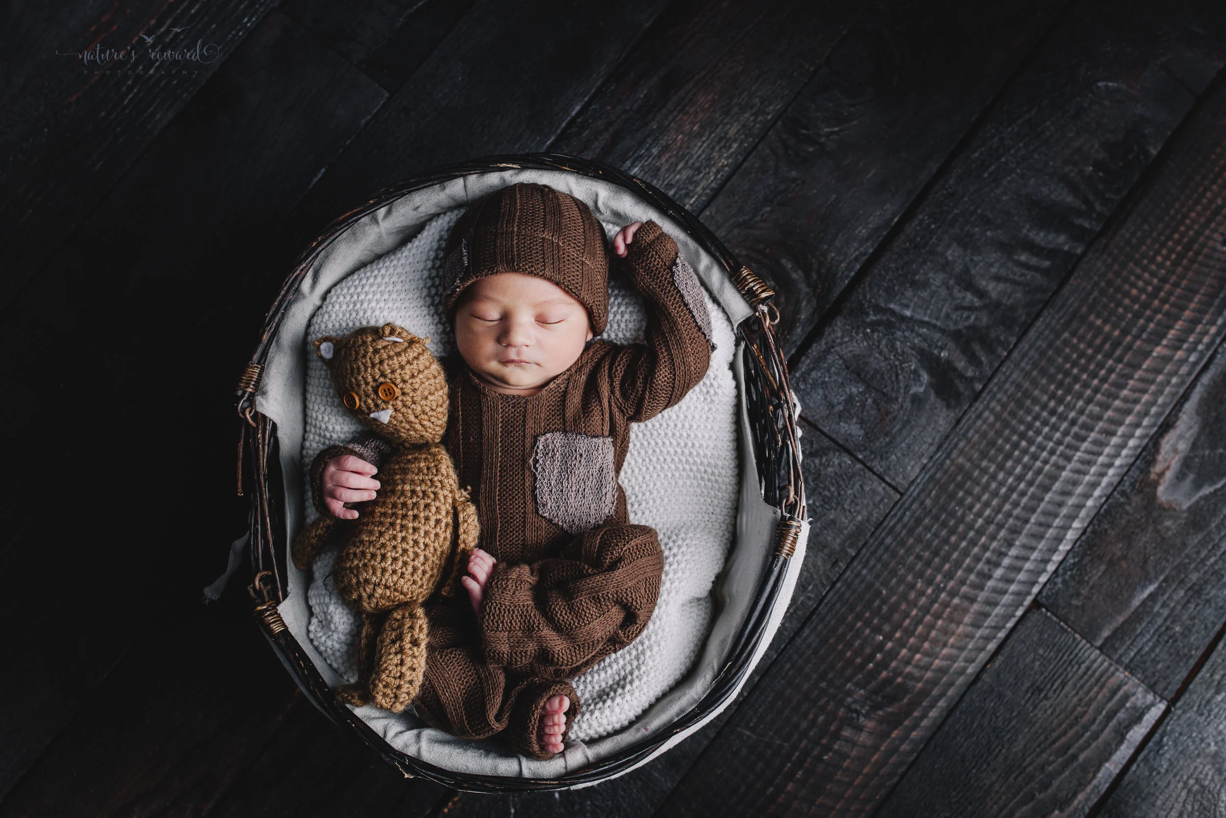 Newborn baby boy portrait wearing a brown outfit and matching cap holding a teddy by Nature’s Reward Photography