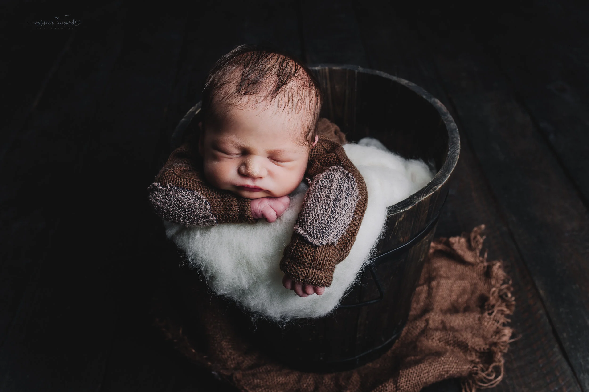 Newborn baby boy portrait wearing a brown outfit in a bucket by Nature’s Reward Photography