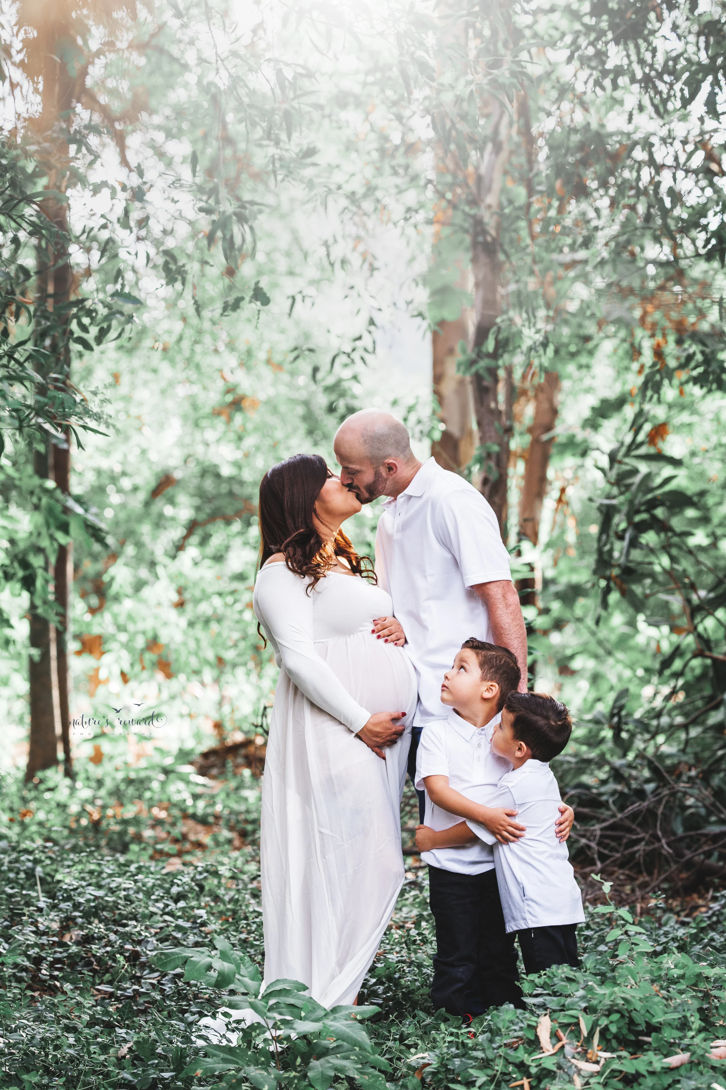 Gorgeous family in whites in a lush green park celebrate the upcoming arrival of their new family member in this lovely maternity session portrait by Nature’s Reward Photography